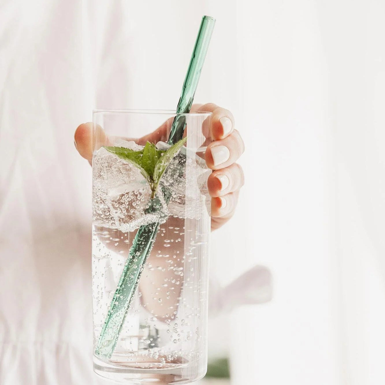 Hand holding green twist glass straw in fizzy drink.