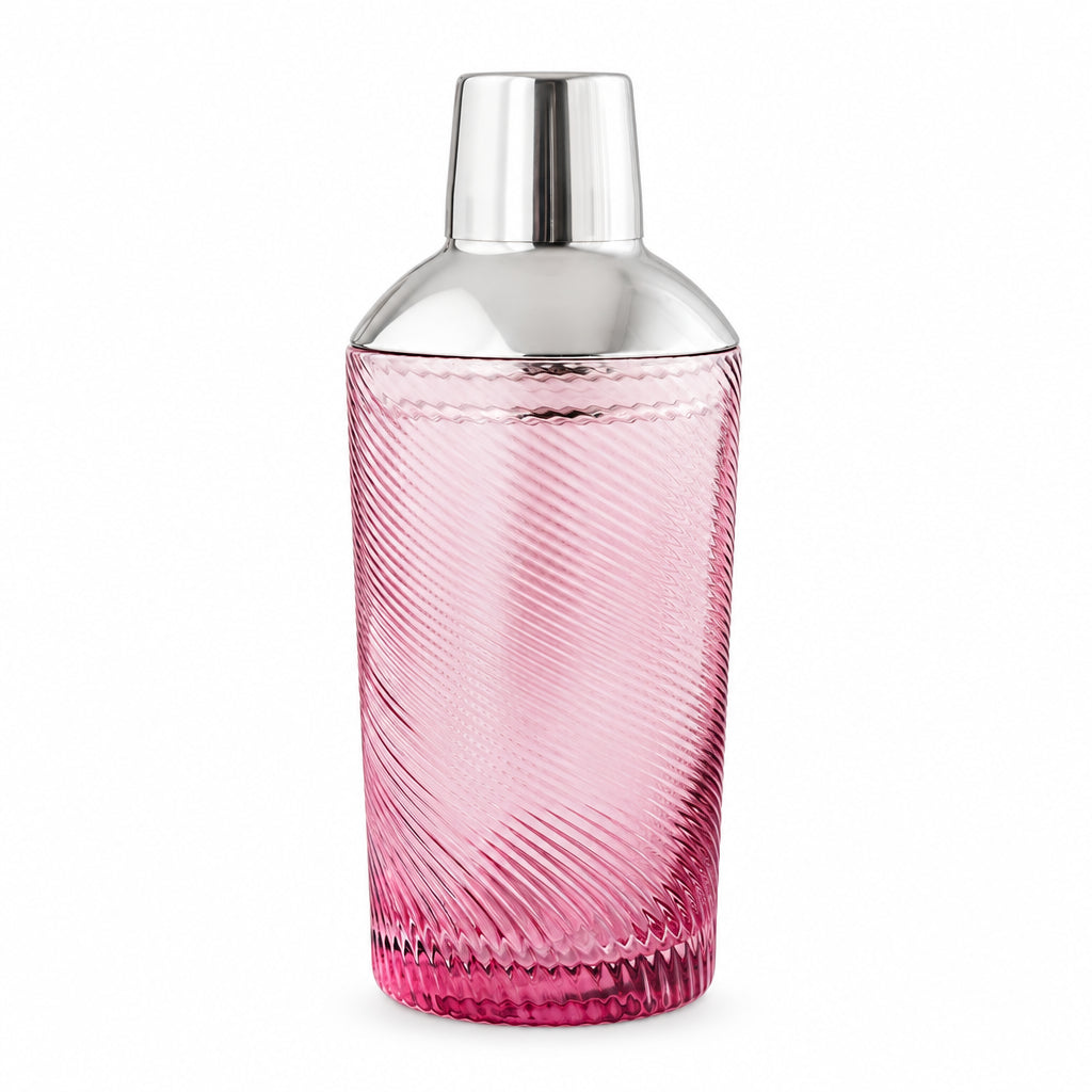Pink glass cocktail shaker with twisted swirl design and shiny steel top, styled with matching glassware and green leaves.