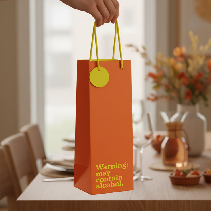 Burnt orange bottle gift bag with yellow warning text held over dining table