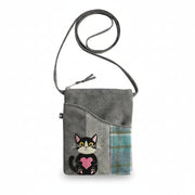A gray fabric crossbody bag with a black leather strap, featuring a patchwork design with a herringbone pattern, a blue plaid pocket, and an embroidered black-and-white cat holding a pink heart.