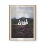Framed artwork of a house in a field with mountains on a beige wall