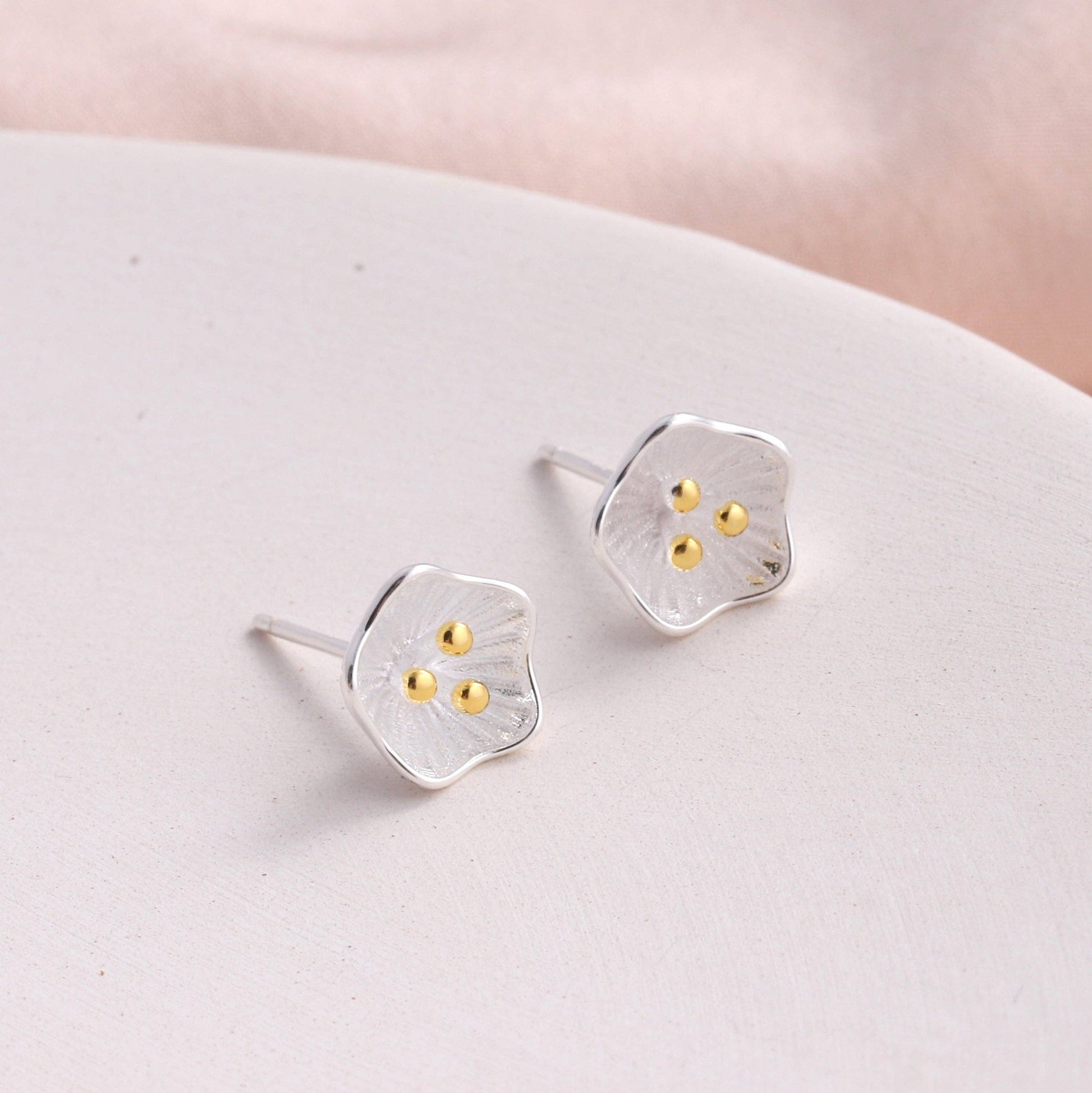 Silver flower stud earrings displayed on cream ceramic plate with light background