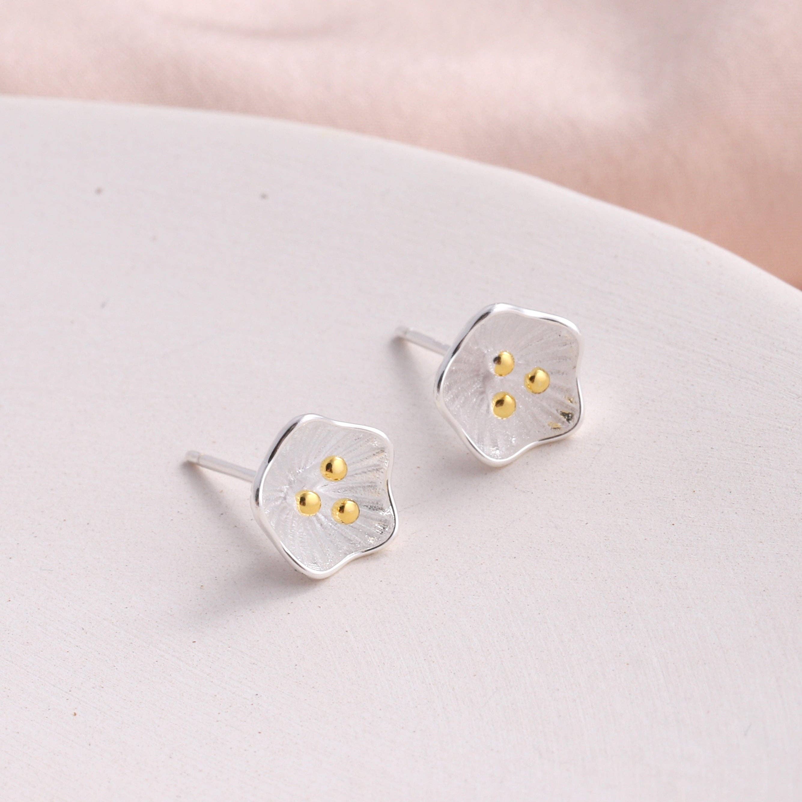 Silver flower stud earrings displayed on cream ceramic plate with light background