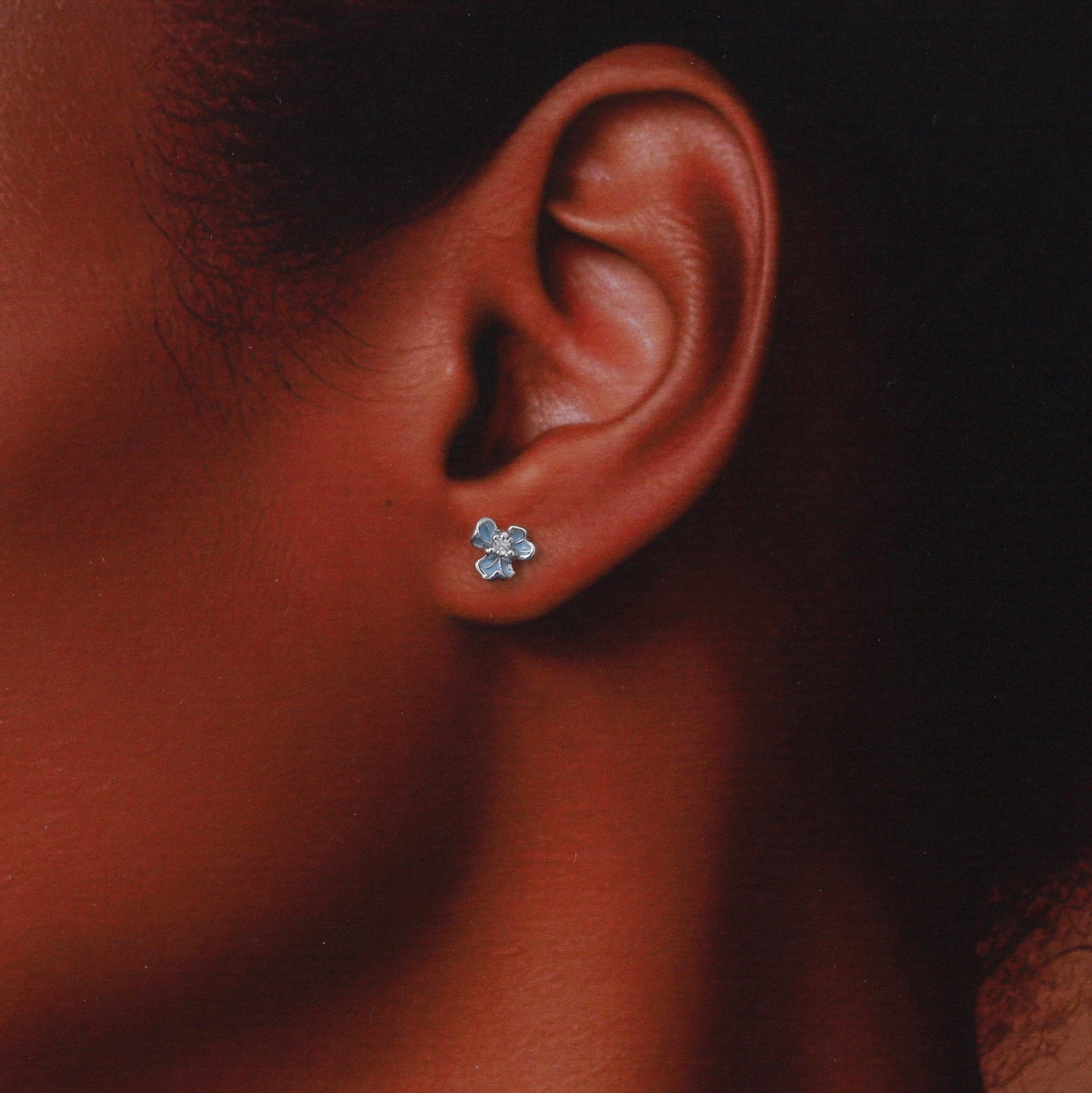 Woman wearing tiny blue flower stud earring in lifestyle close-up