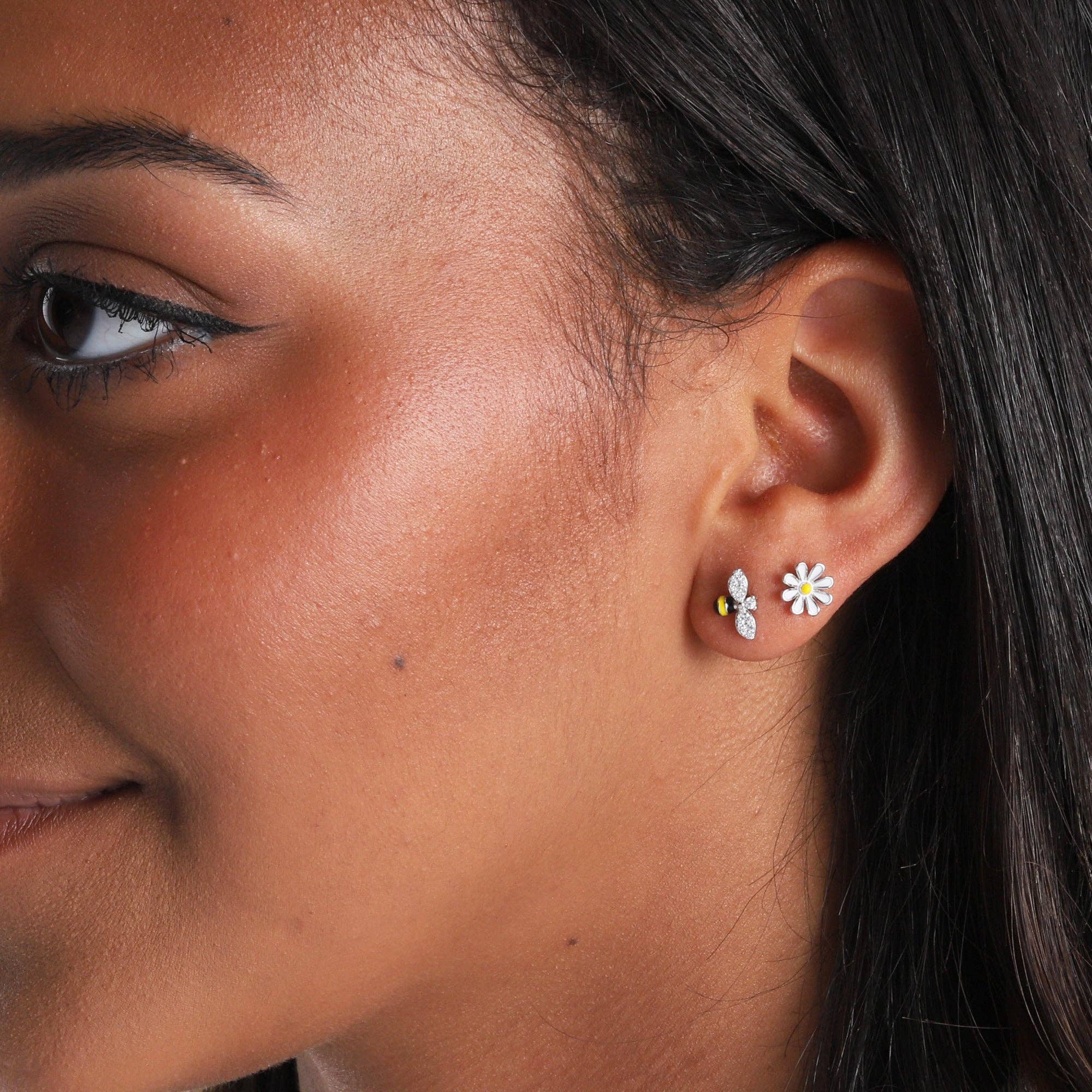 Woman wearing silver bee and flower mismatched stud earring close-up