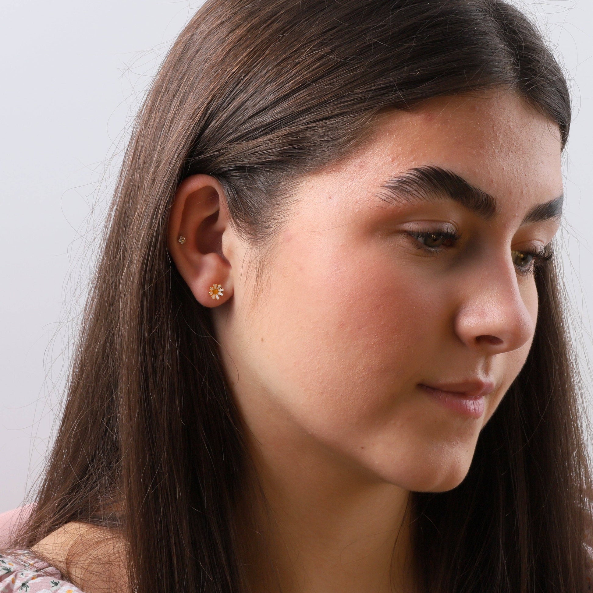 Woman wearing gold enamel daisy stud earring in lifestyle close-up