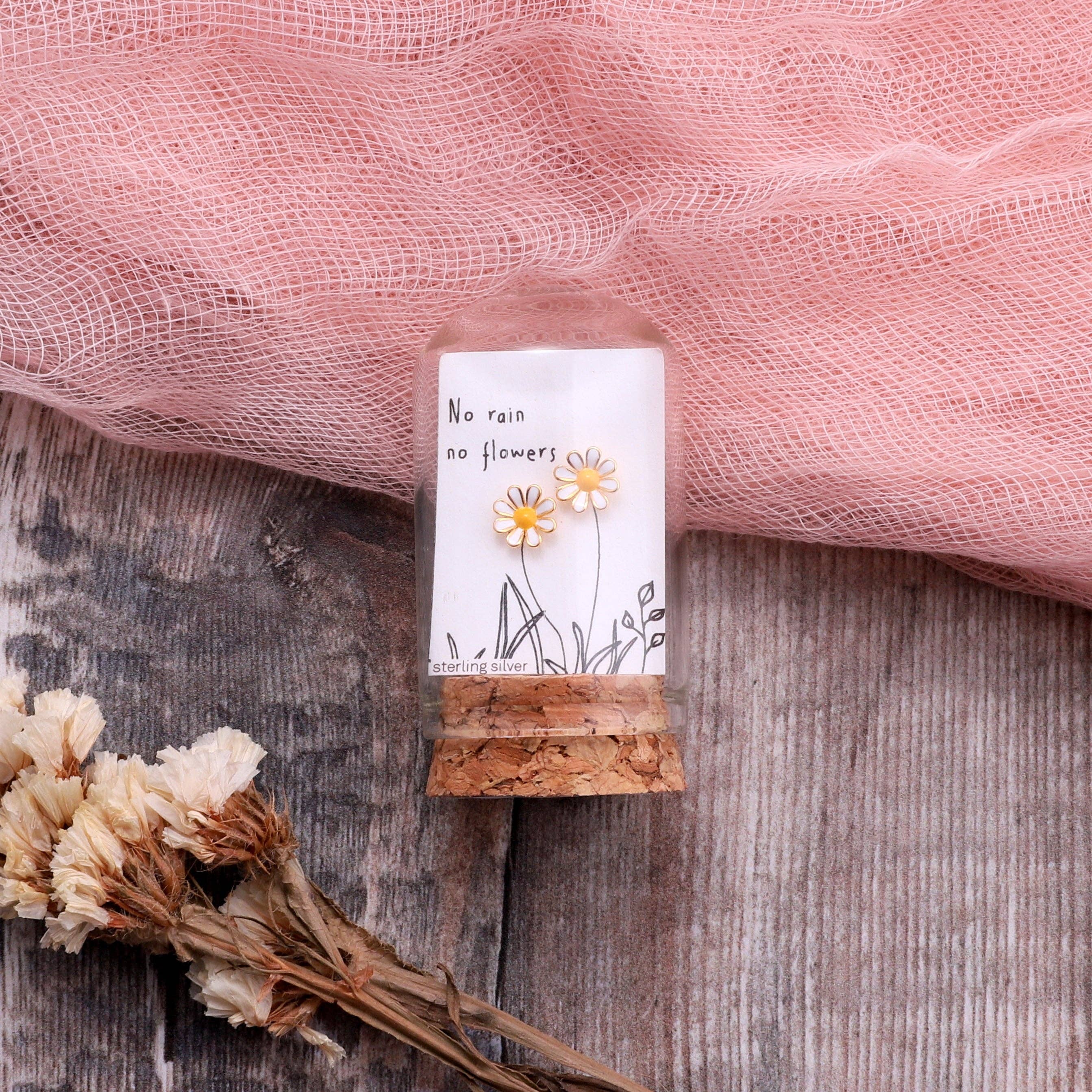 Gold enamel daisy earrings on message card inside glass terrarium held in hand