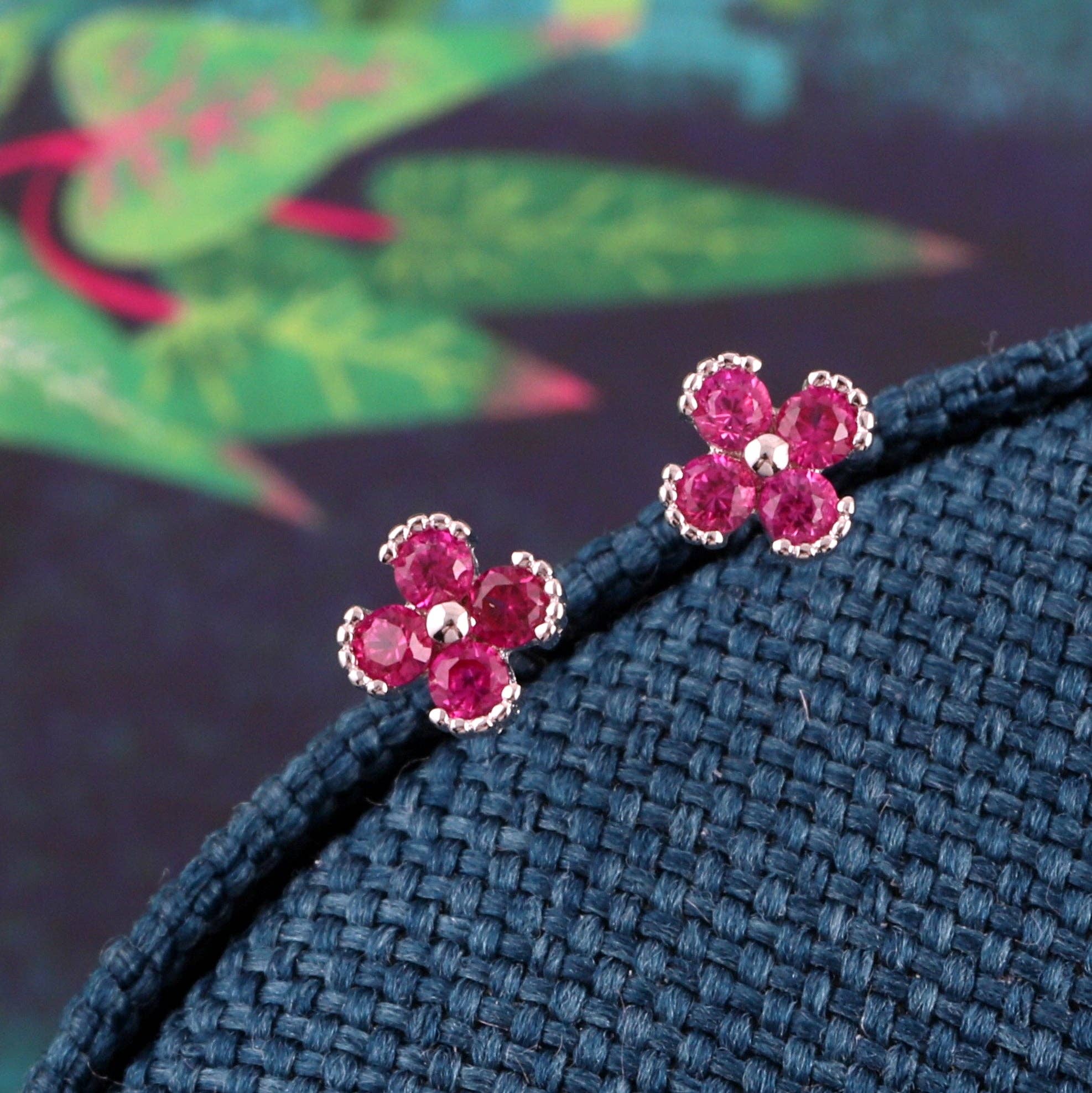Pink and purple gem flower stud earrings displayed on fresh green leaves