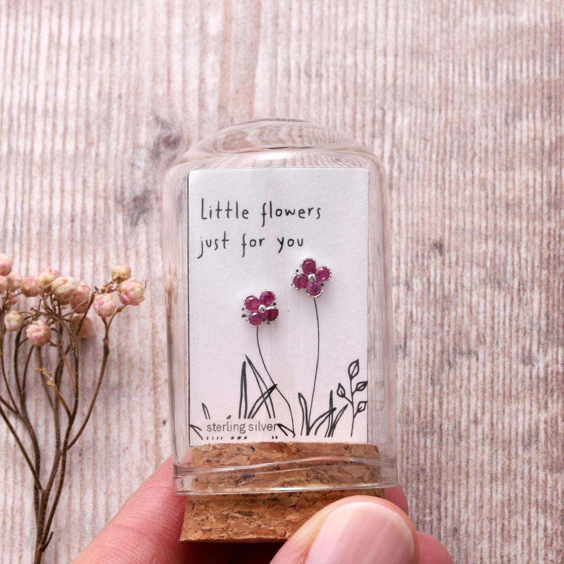 Silver gem flower stud earrings on message card inside glass terrarium held in hand