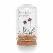 Small glass container with dried flowers and a label on a textured surface