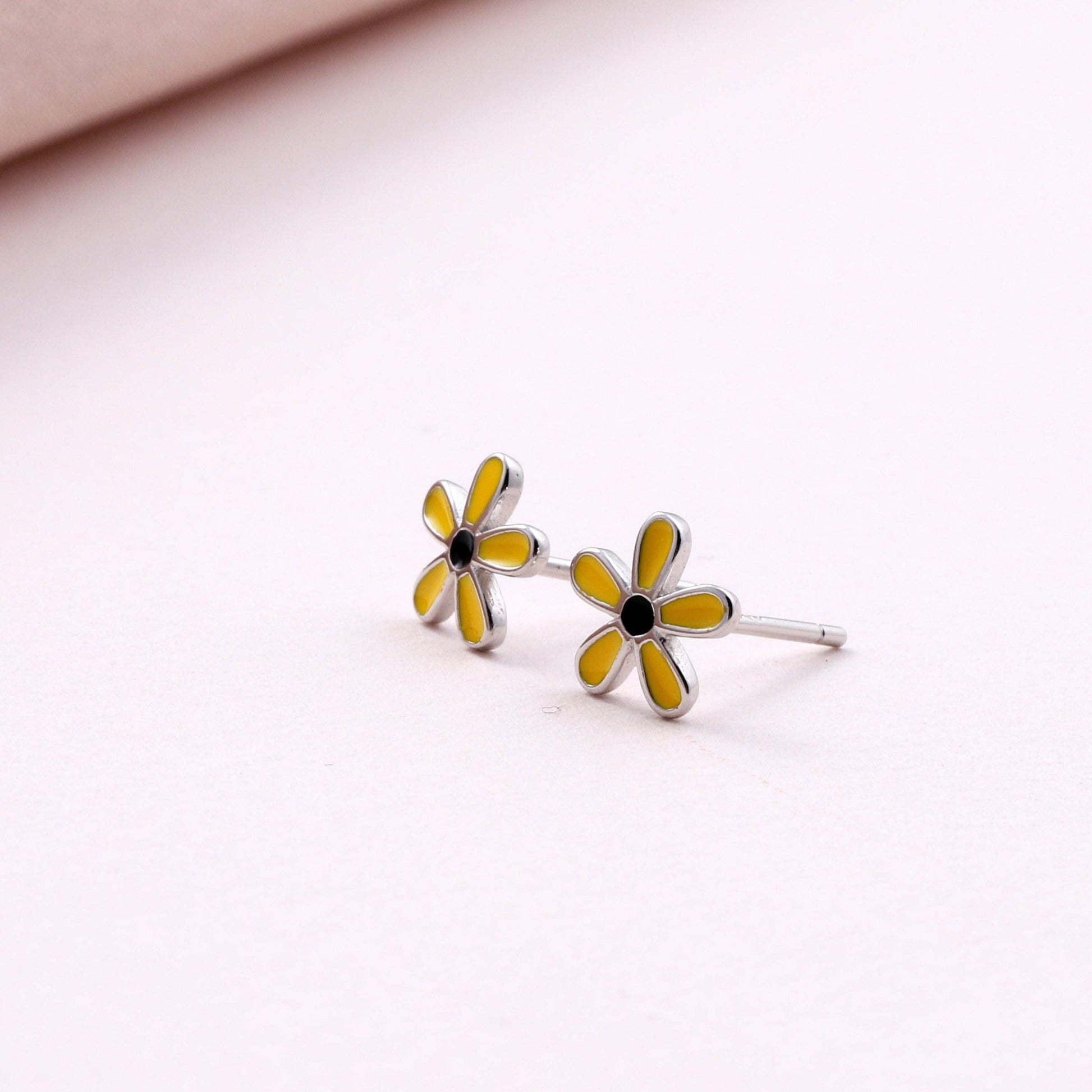 Two yellow enamel daisy stud earrings close-up on white background