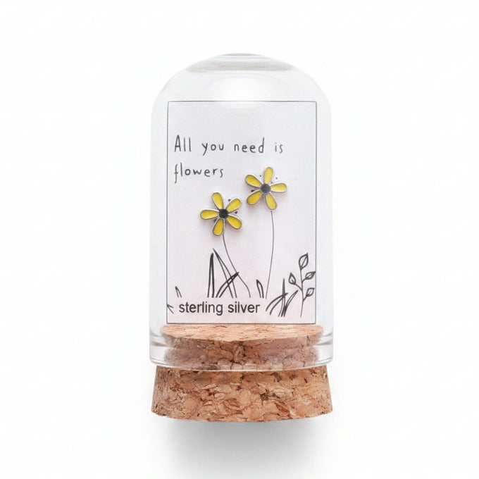Small glass bottle with cork lid containing flowers, held over a cardboard box with floral elements.