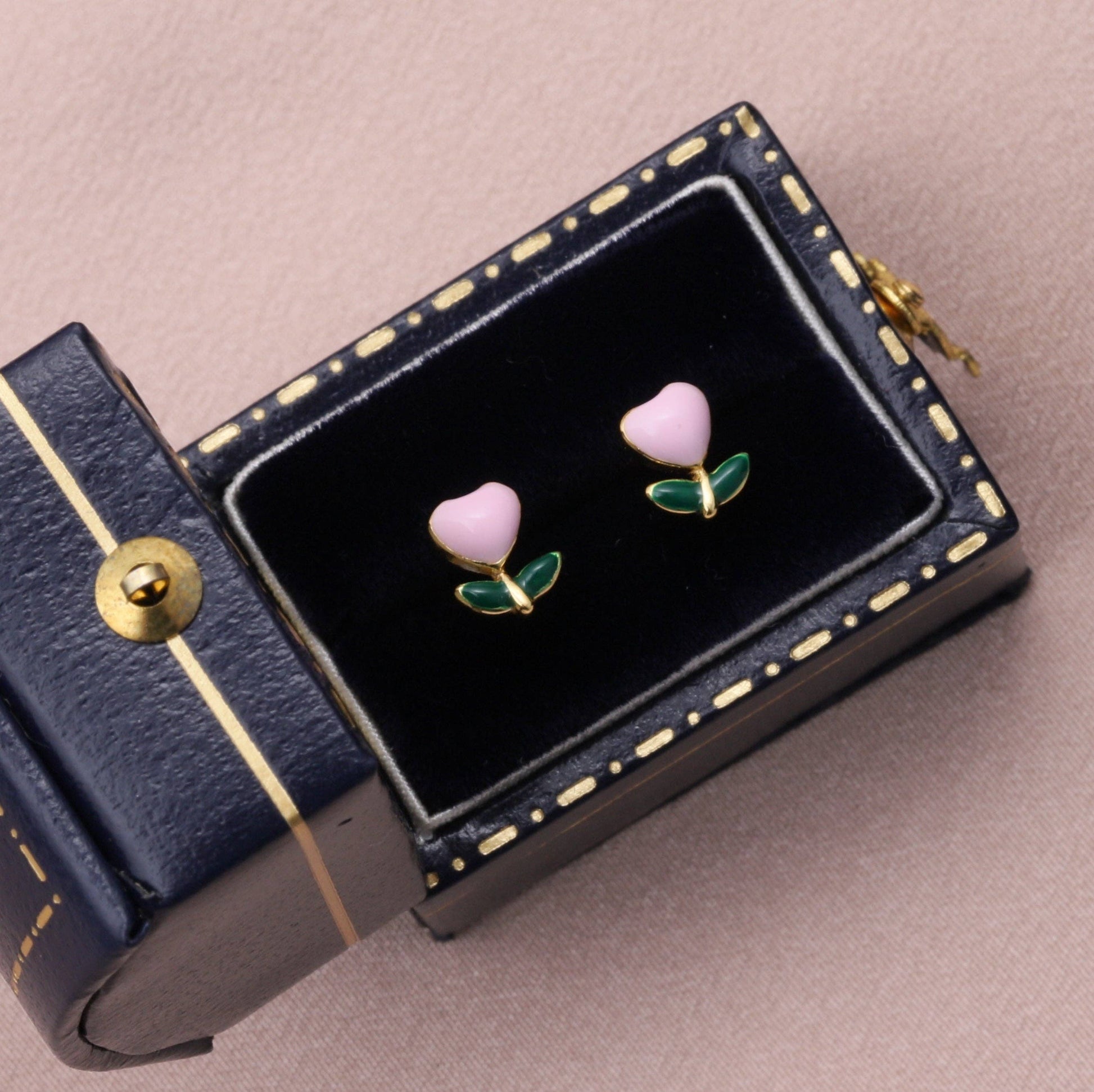 Pink enamel flower stud earrings on dark navy jewellery box with gold trim