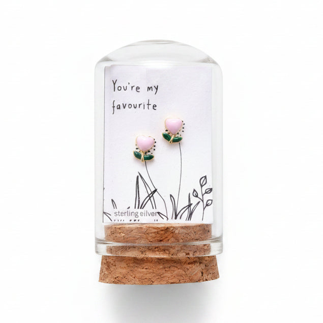 Pink enamel flower earrings in glass terrarium held in hand on grey wooden background