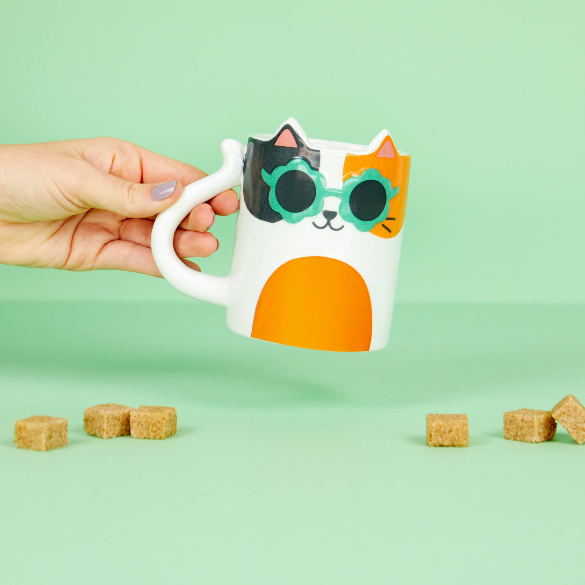 Hand holding the Cool Cat mug showing the tail-shaped handle, green background