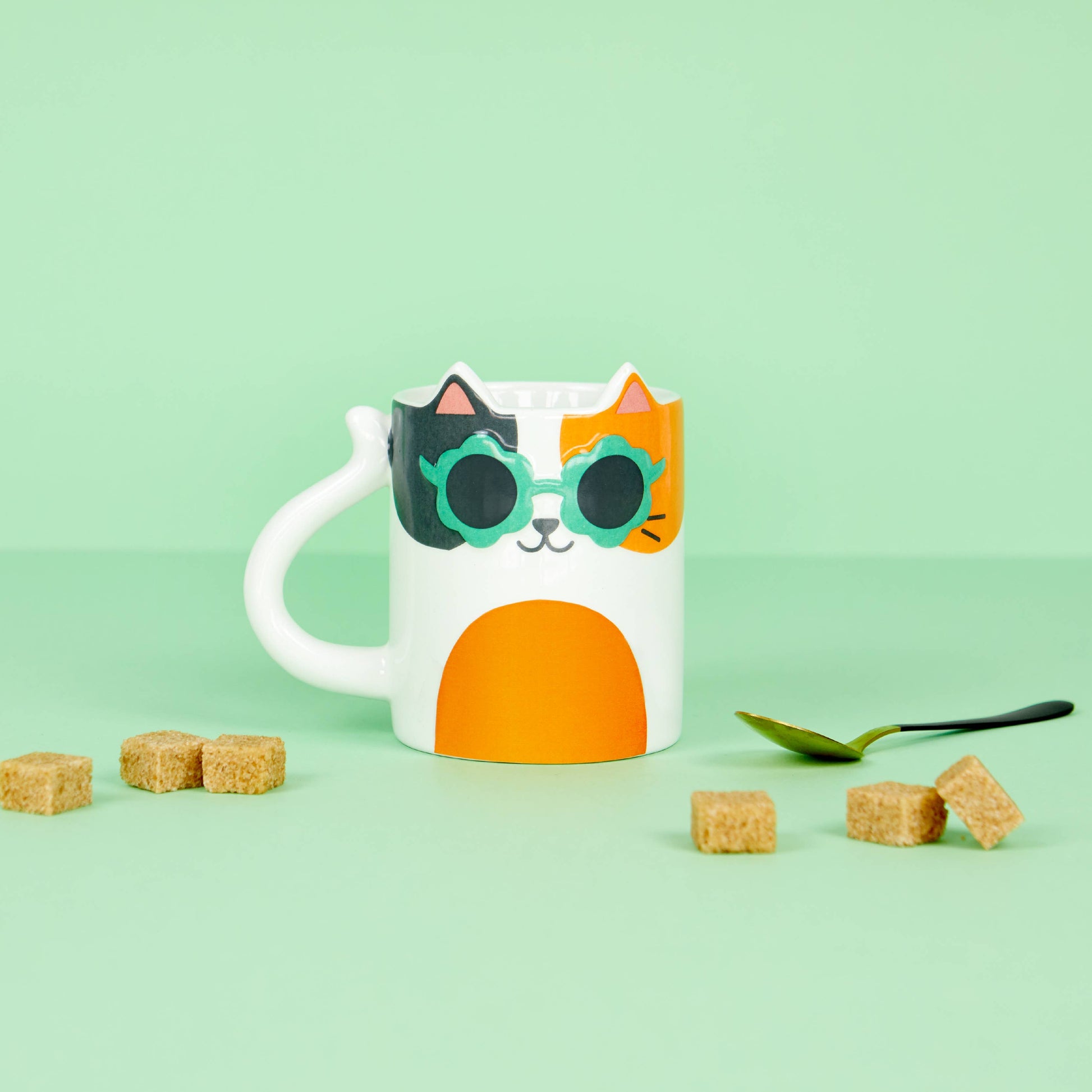 Cool Cat mug styled on a green background with sugar cubes and a spoon