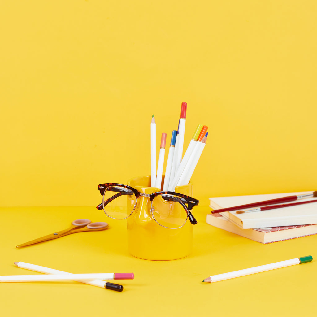 Mustard nose pen holder with pencils, scissors and notebooks on a yellow desk