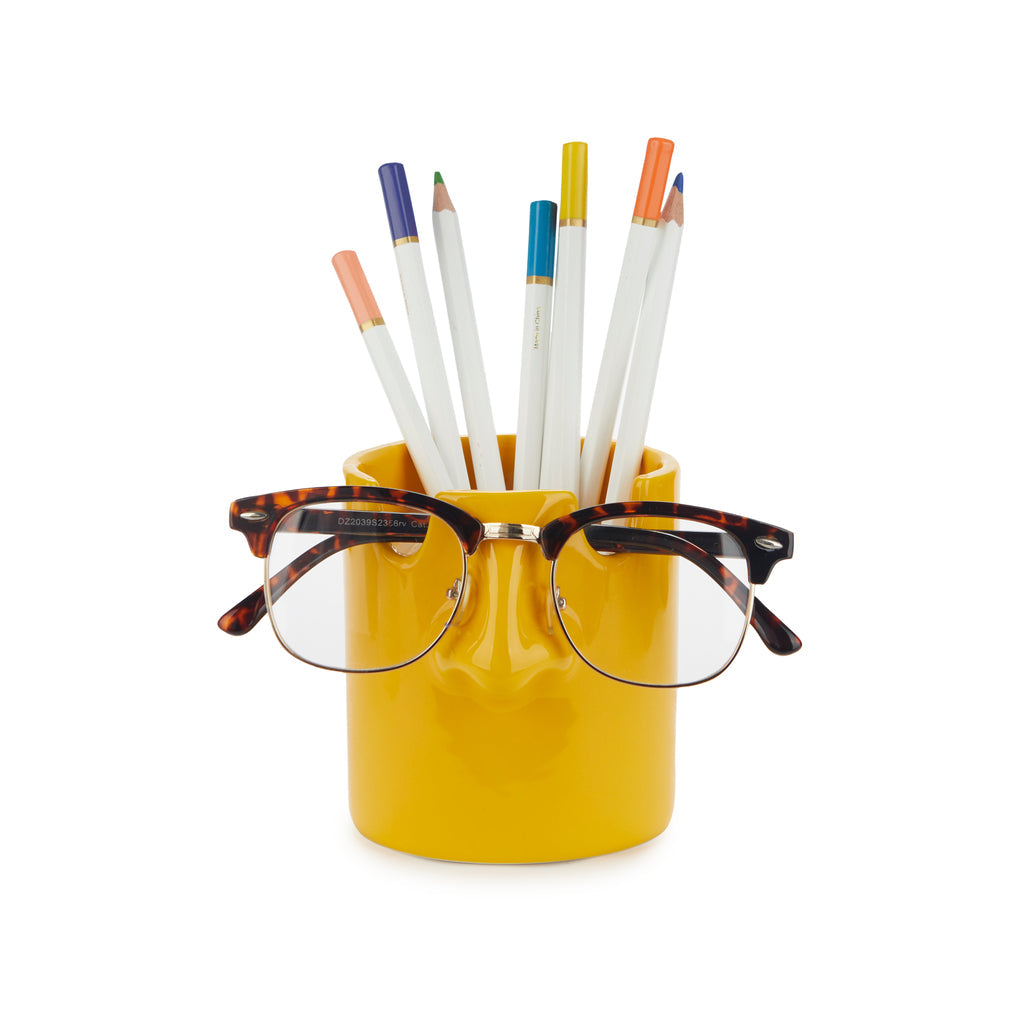 Mustard yellow nose pen holder with coloured pencils and glasses on white