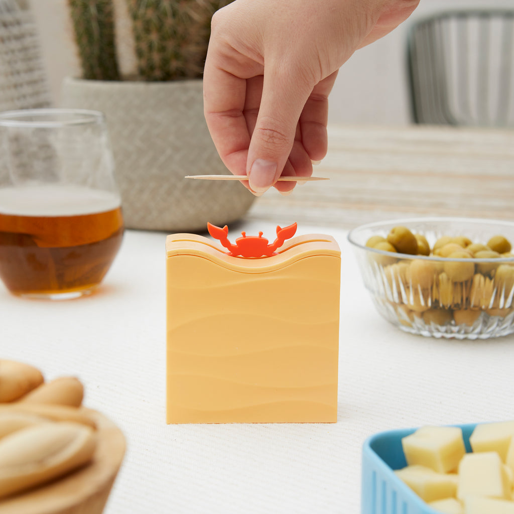 Hand lifting a toothpick from the crab dispenser beside olives and a beer