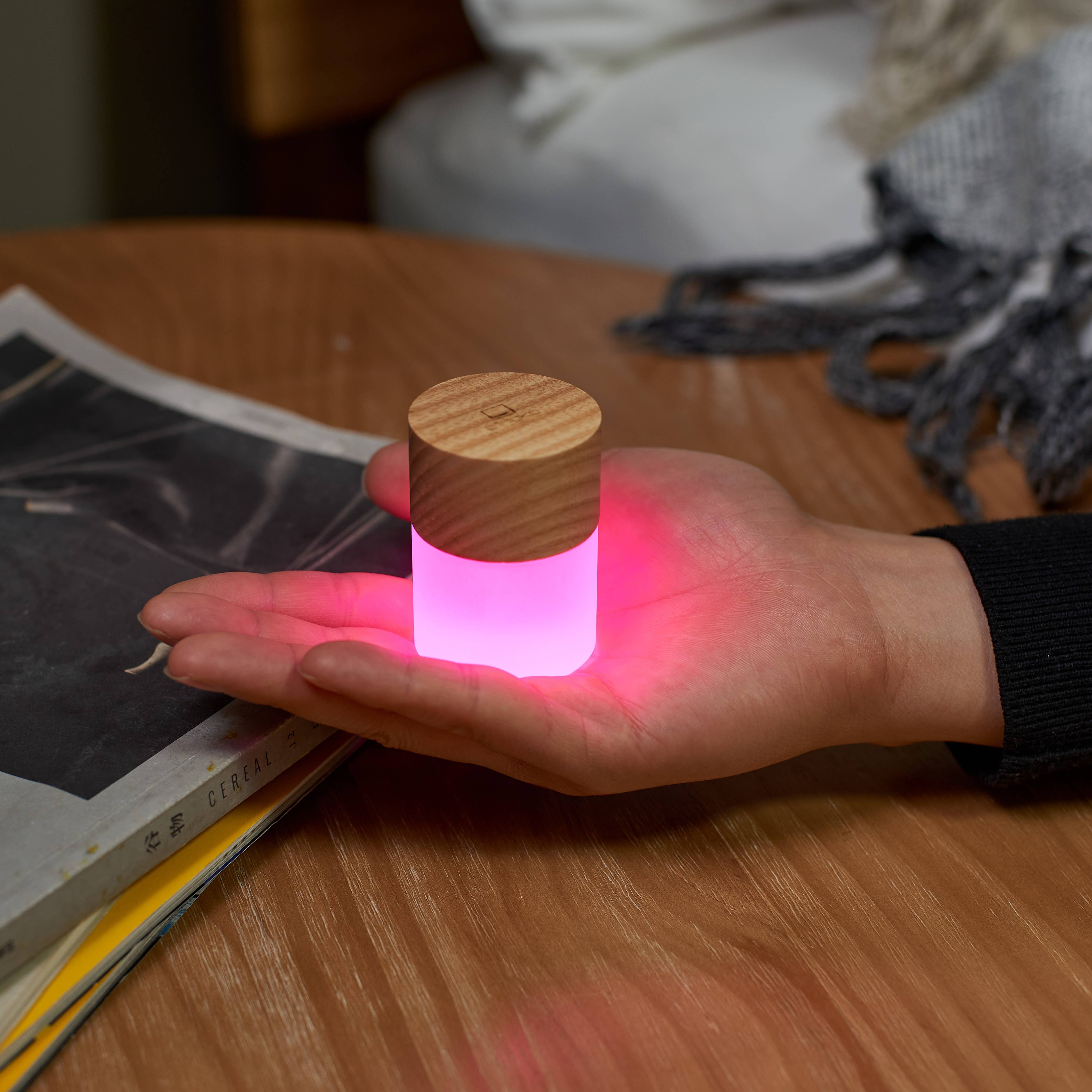 Lemelia mini light with light wood top glowing pink in a cupped hand