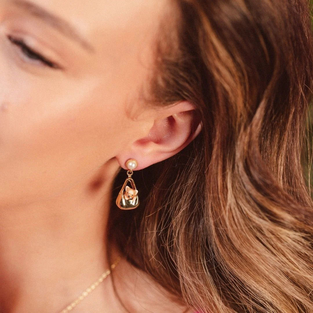 Model wearing Bill Skinner Dog in a Bag Drop Earrings with gold finish and pearl stud detail.