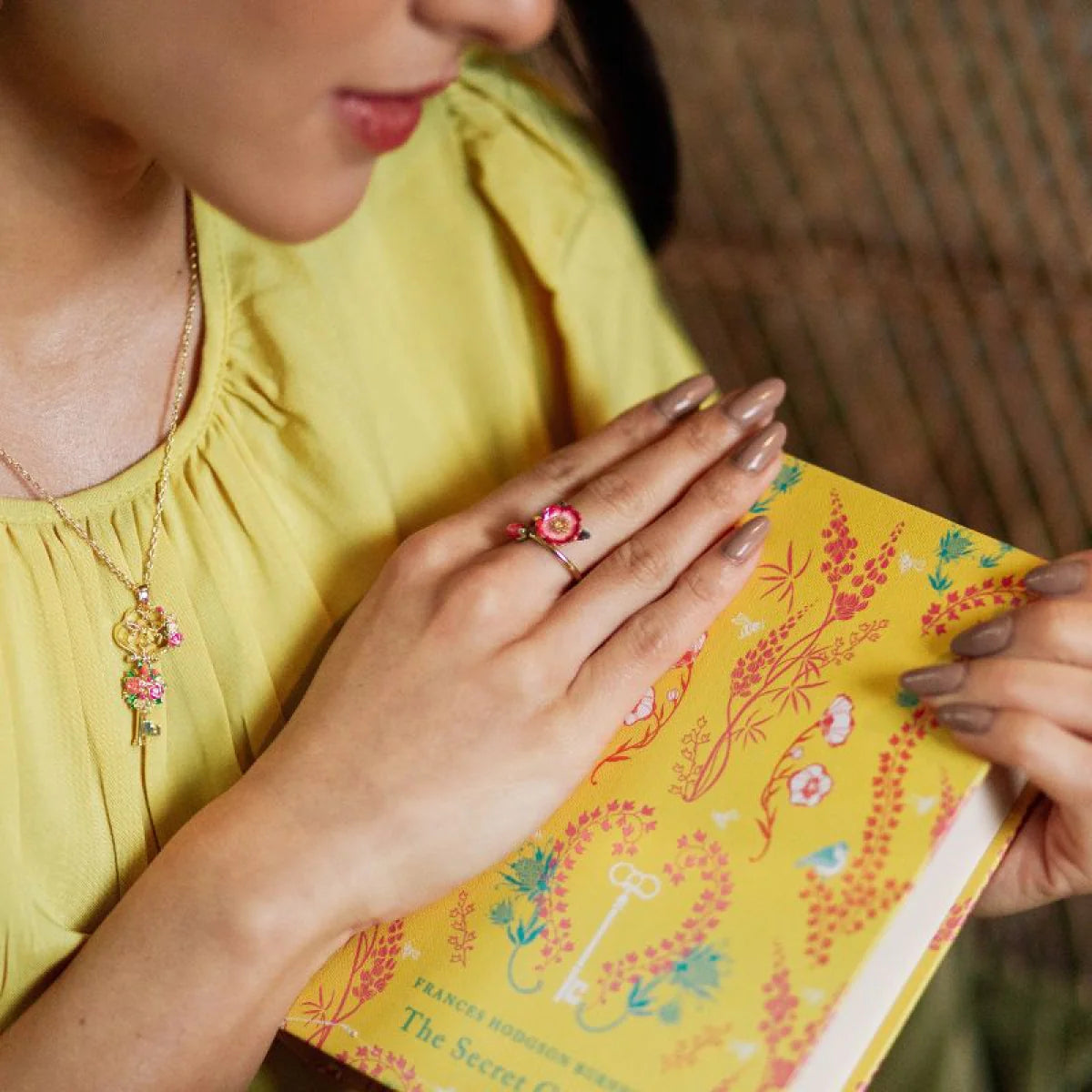 Model reading with Bill Skinner Wild Flower Open Ring on hand, paired with matching floral necklace for a coordinated look.