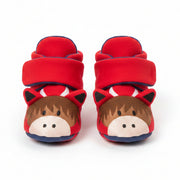 A close-up of a child's feet wearing red slipper-on slippers shaped like highland cows, paired with gray and navy striped tights.
