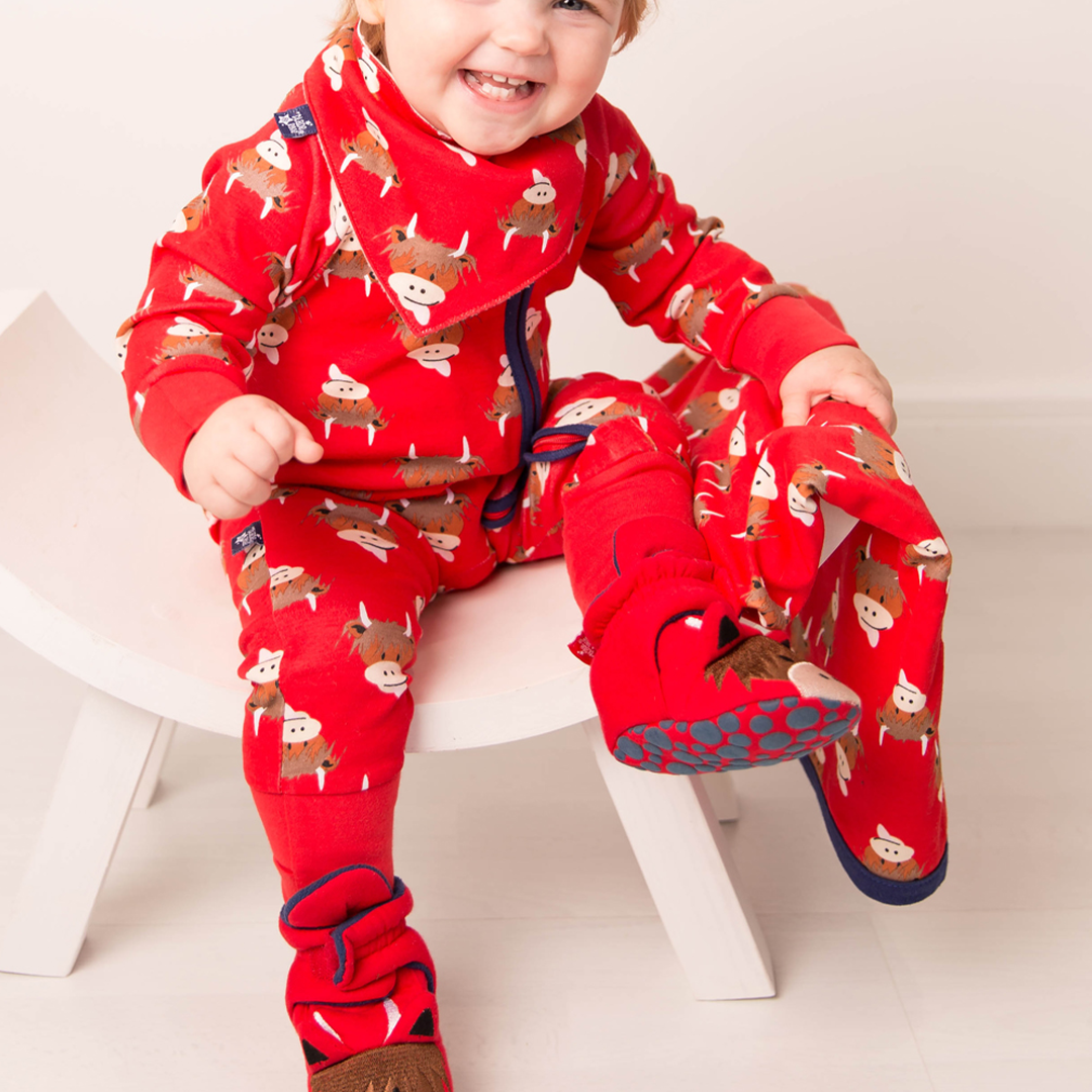 Baby seated wearing red highland cow zip-up romper