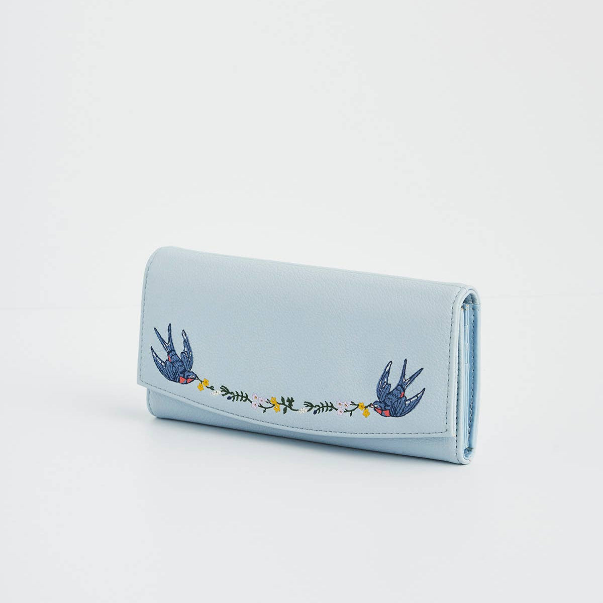 Angled view of light blue embroidered bird purse with foldover flap.