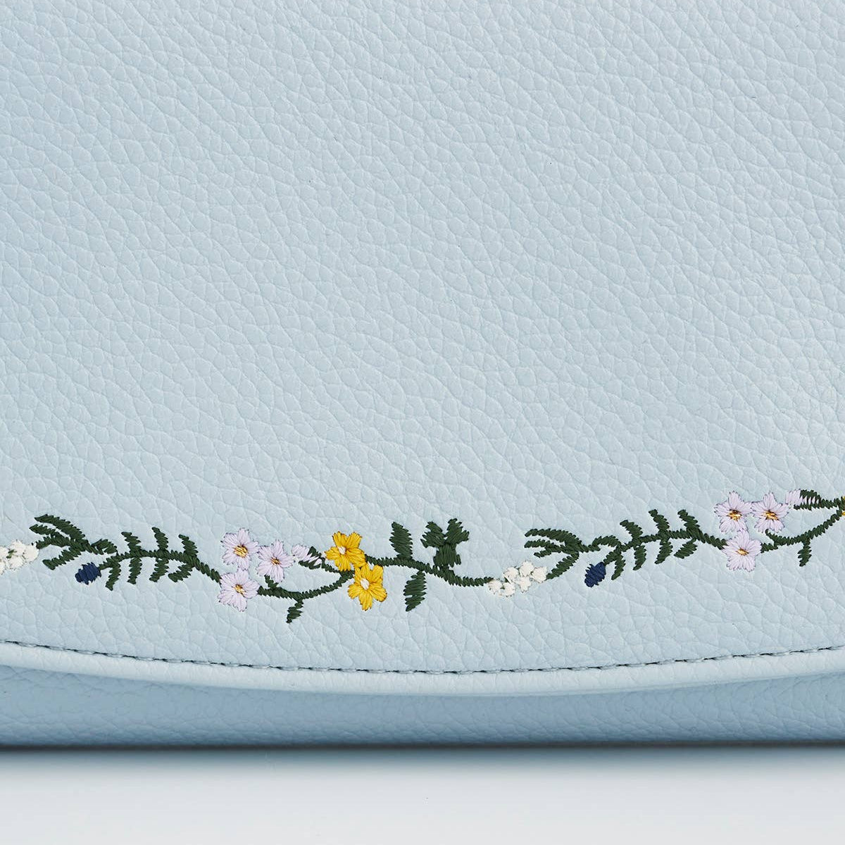 Close up of floral embroidery on the light blue purse flap.
