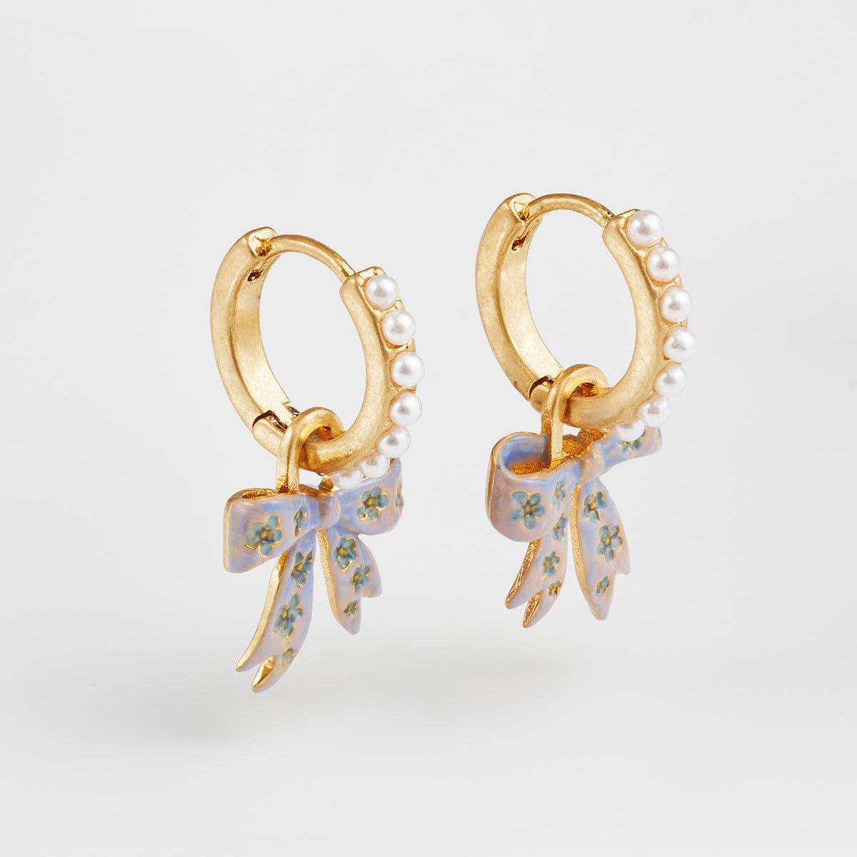 Front view of the gold huggie earrings with pearl detail and bow charms.