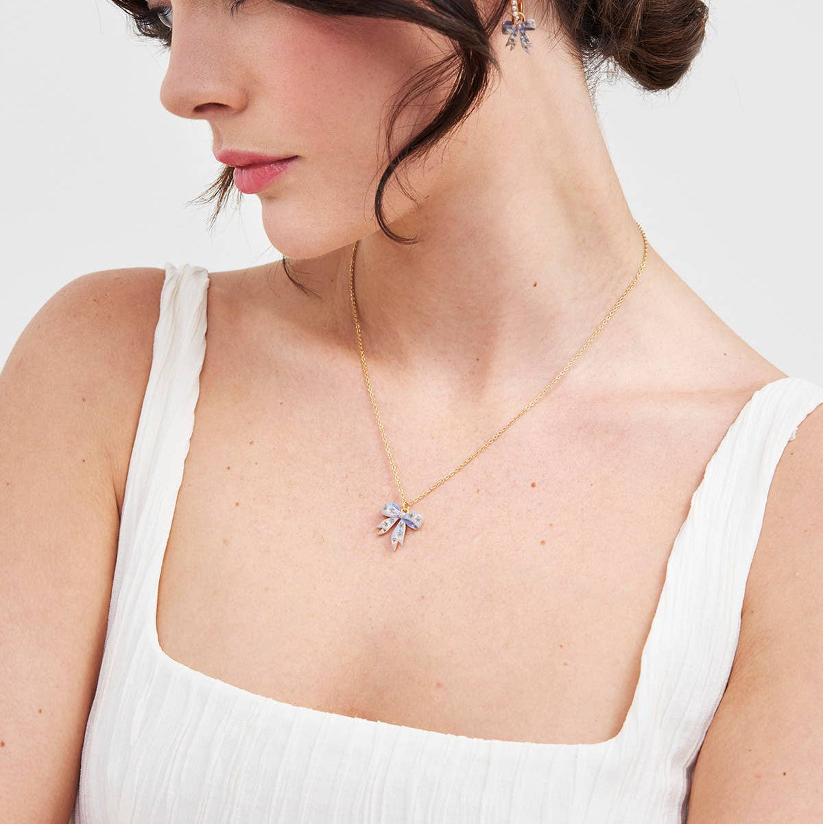 Model wearing gold bow pendant necklace.