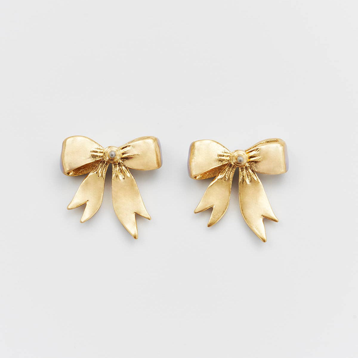 Gold bow stud earrings with central bead detail on white background