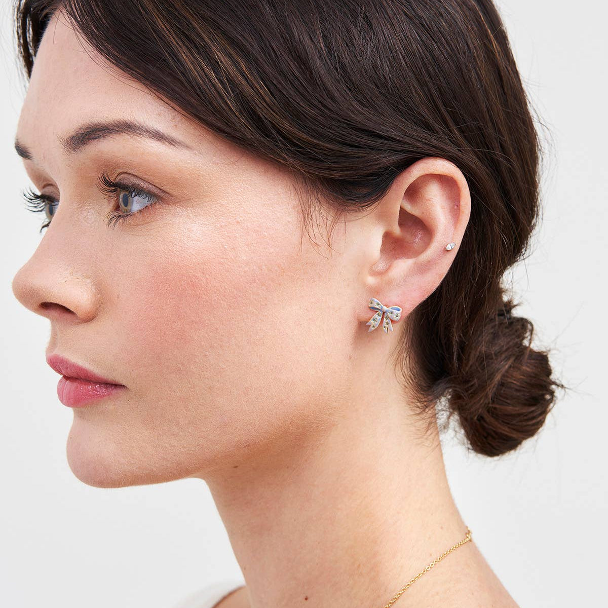 Model wearing gold bow stud earrings with delicate enamel finish