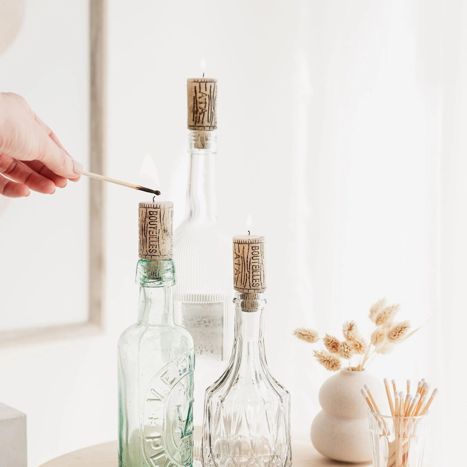 Burning wine cork candles displayed in glass bottles.