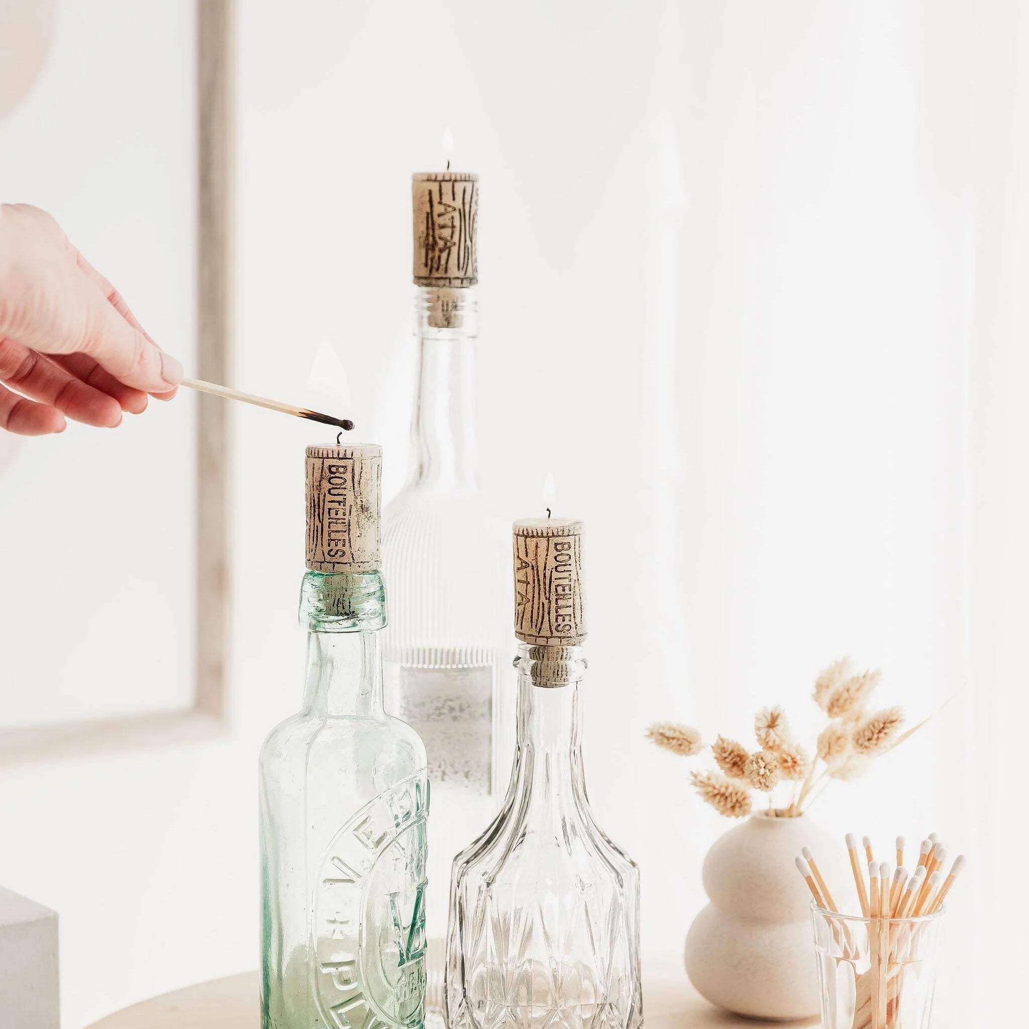 Burning wine cork candles displayed in glass bottles.