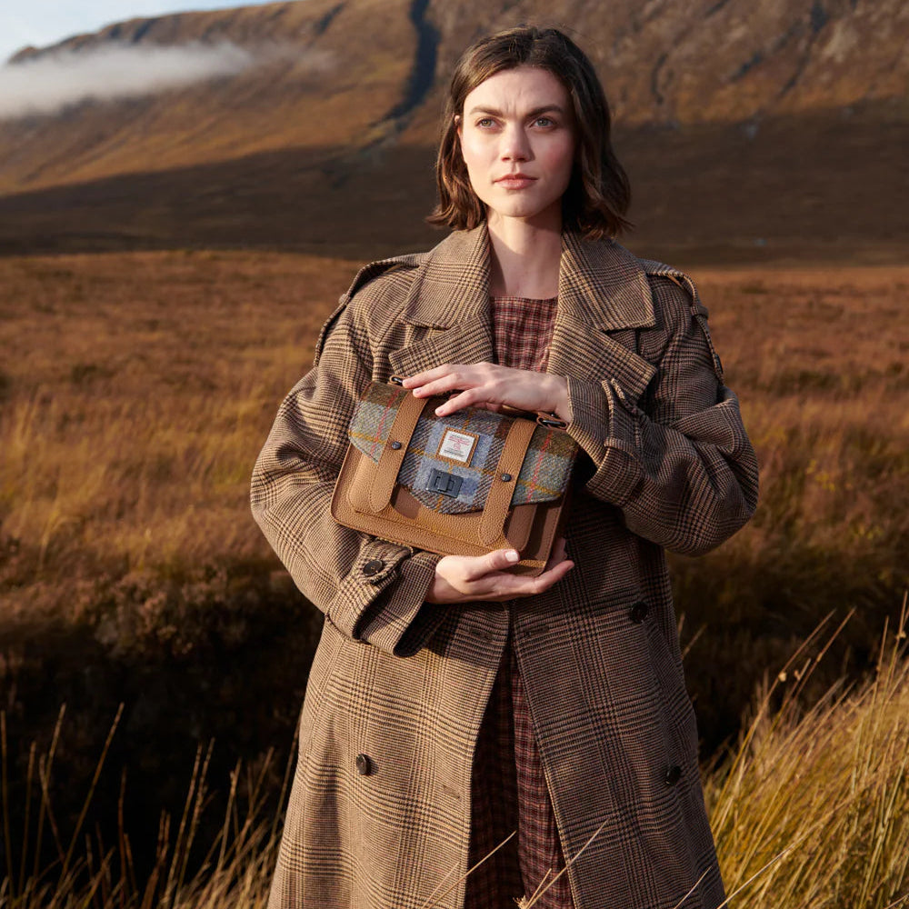 Lifestyle image of chestnut and blue Harris Tweed leather satchel held outdoors in Scotland.