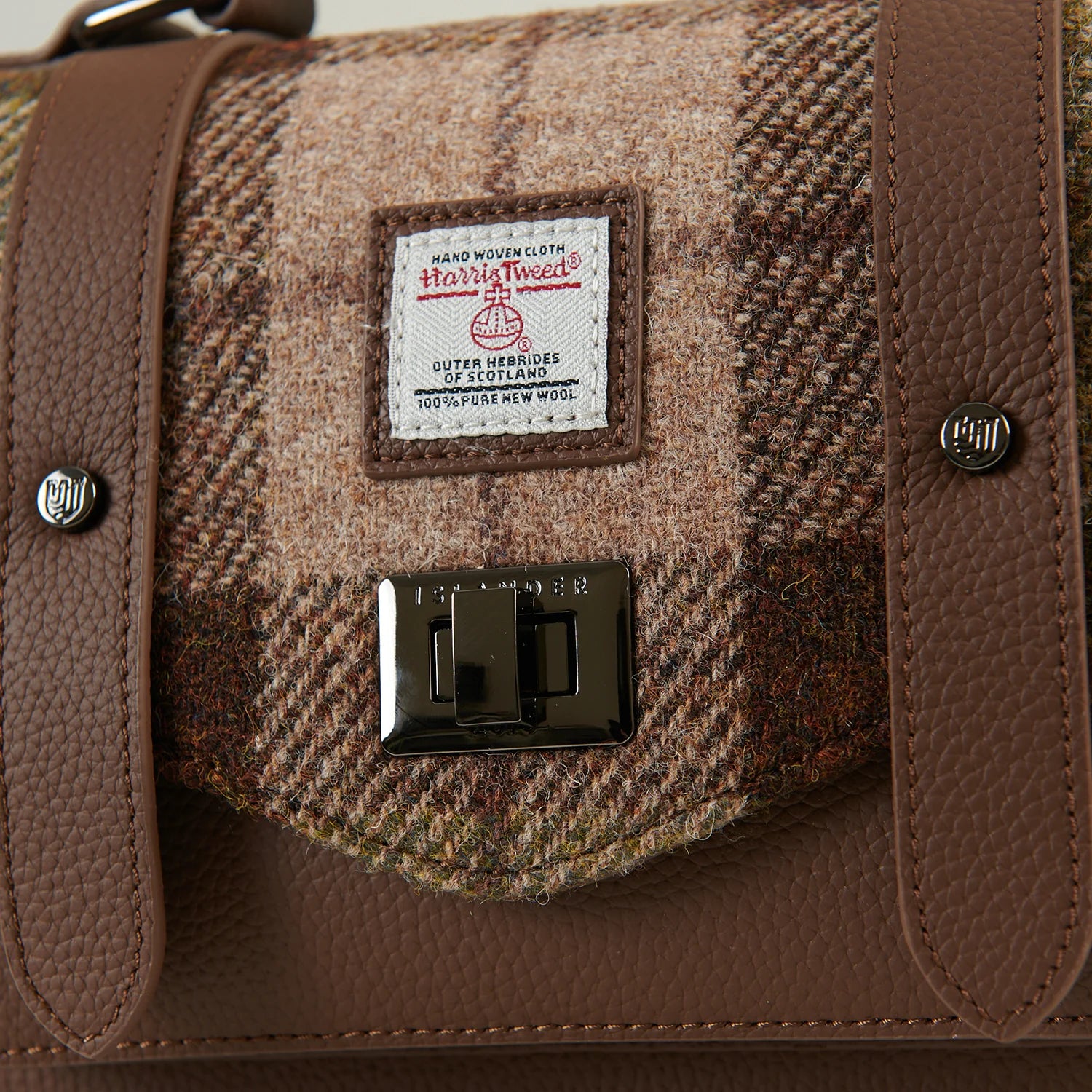 Close-up of chestnut tartan Harris Tweed fabric with leather straps and metal clasp.
