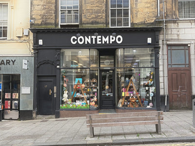 A storefront for the brand CONTEMPO onStirling King street, with a black facade, large white lettering, glass windows displaying merchandise, and a wooden bench on the sidewalk in front.
