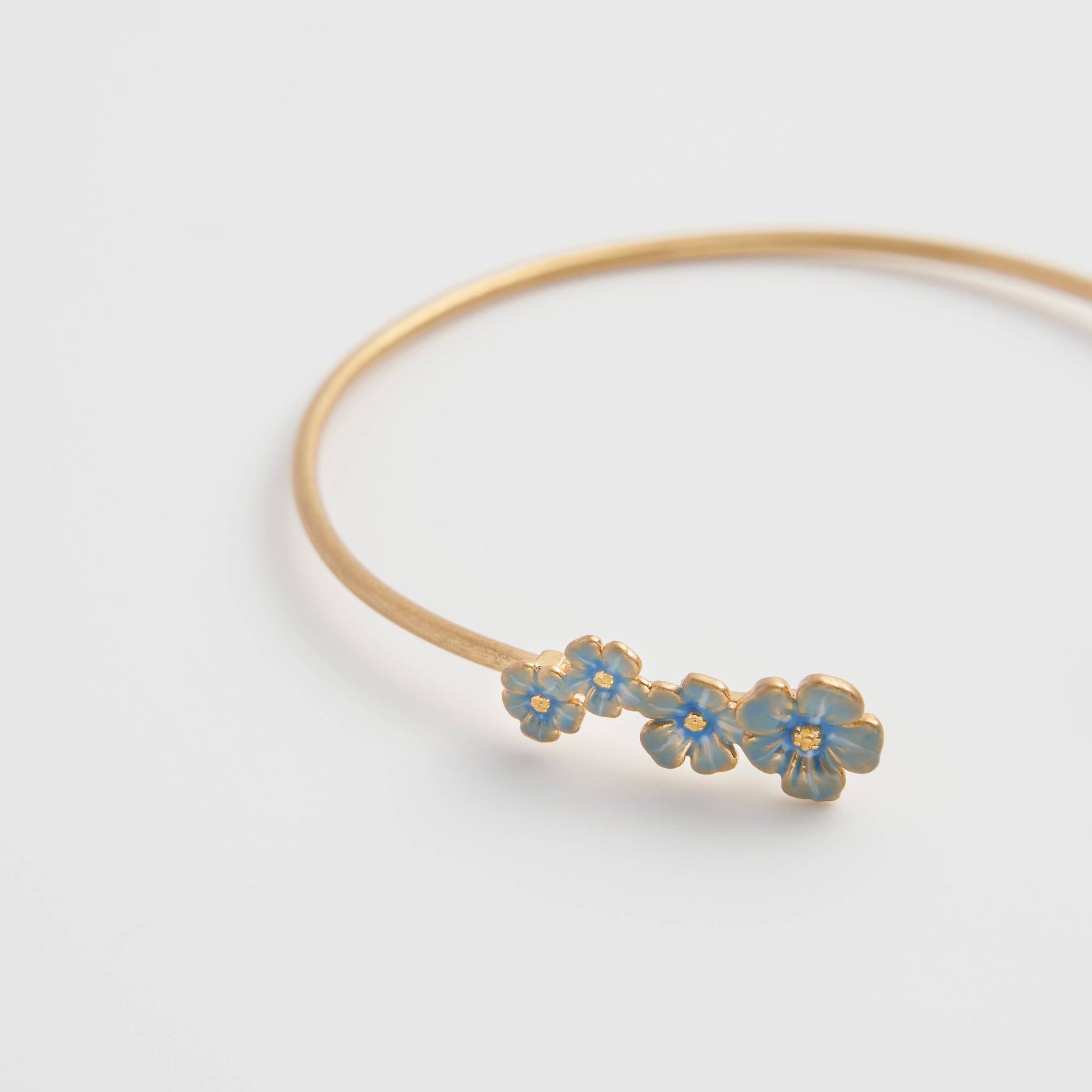 Delicate forget-me-not bangle with hand-painted blue enamel flowers and gold-plated finish on white background