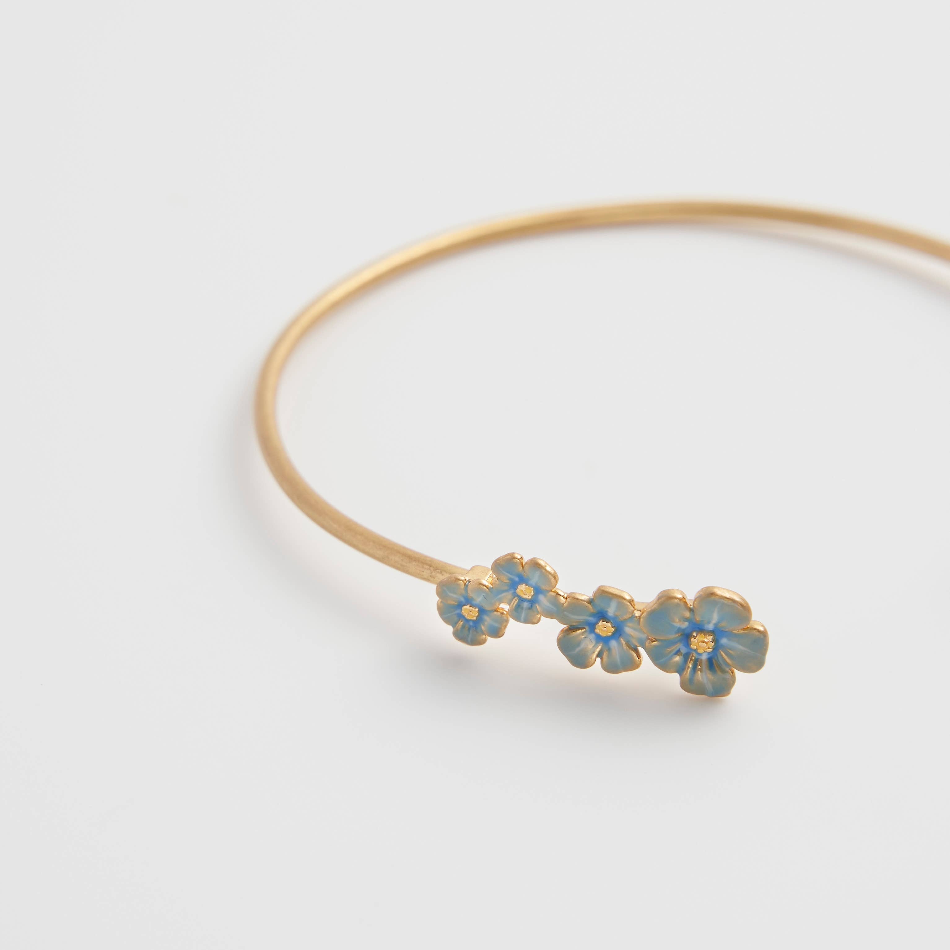Delicate forget-me-not bangle with hand-painted blue enamel flowers and gold-plated finish on white background