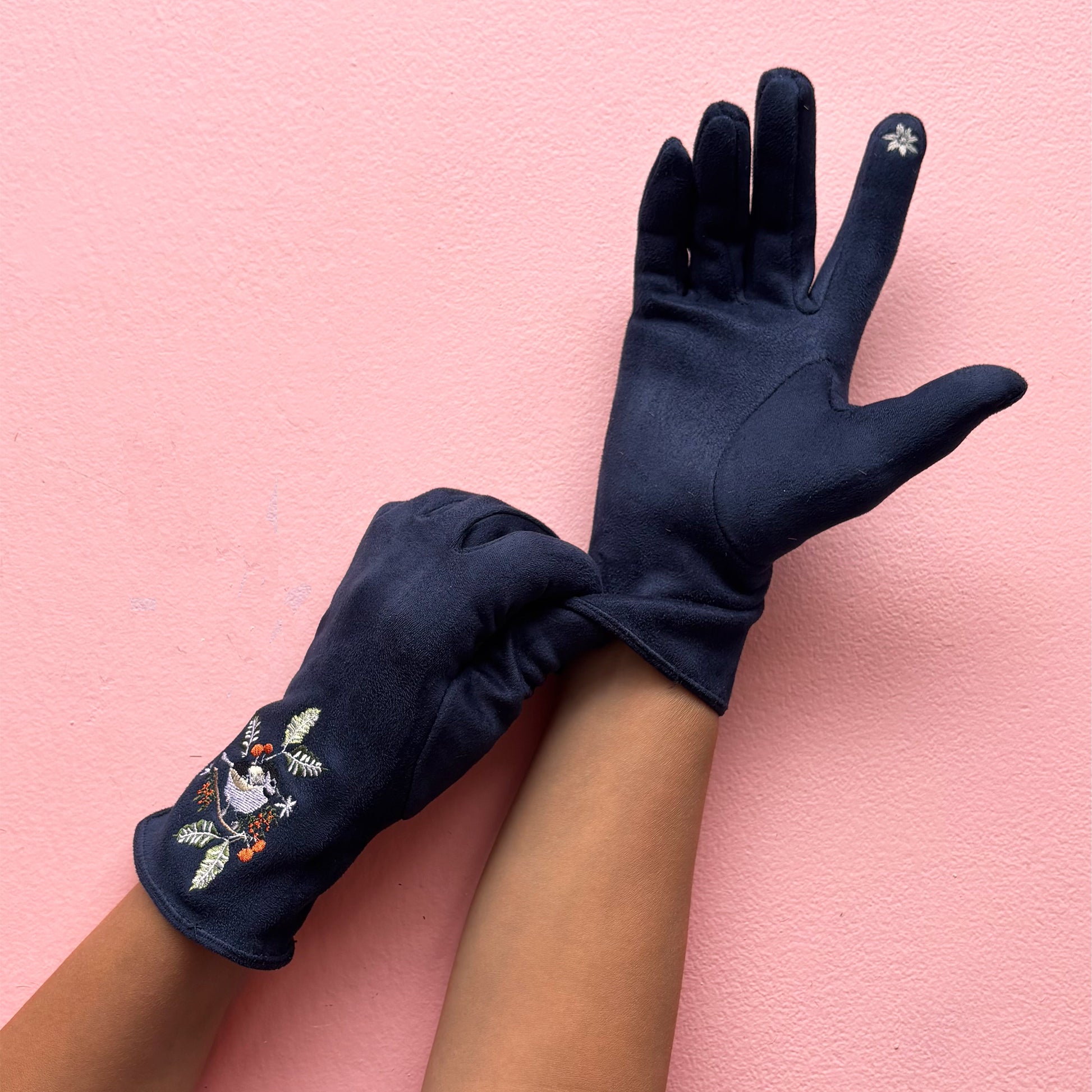 Single navy bird glove on pink background with greenery showing embroidery