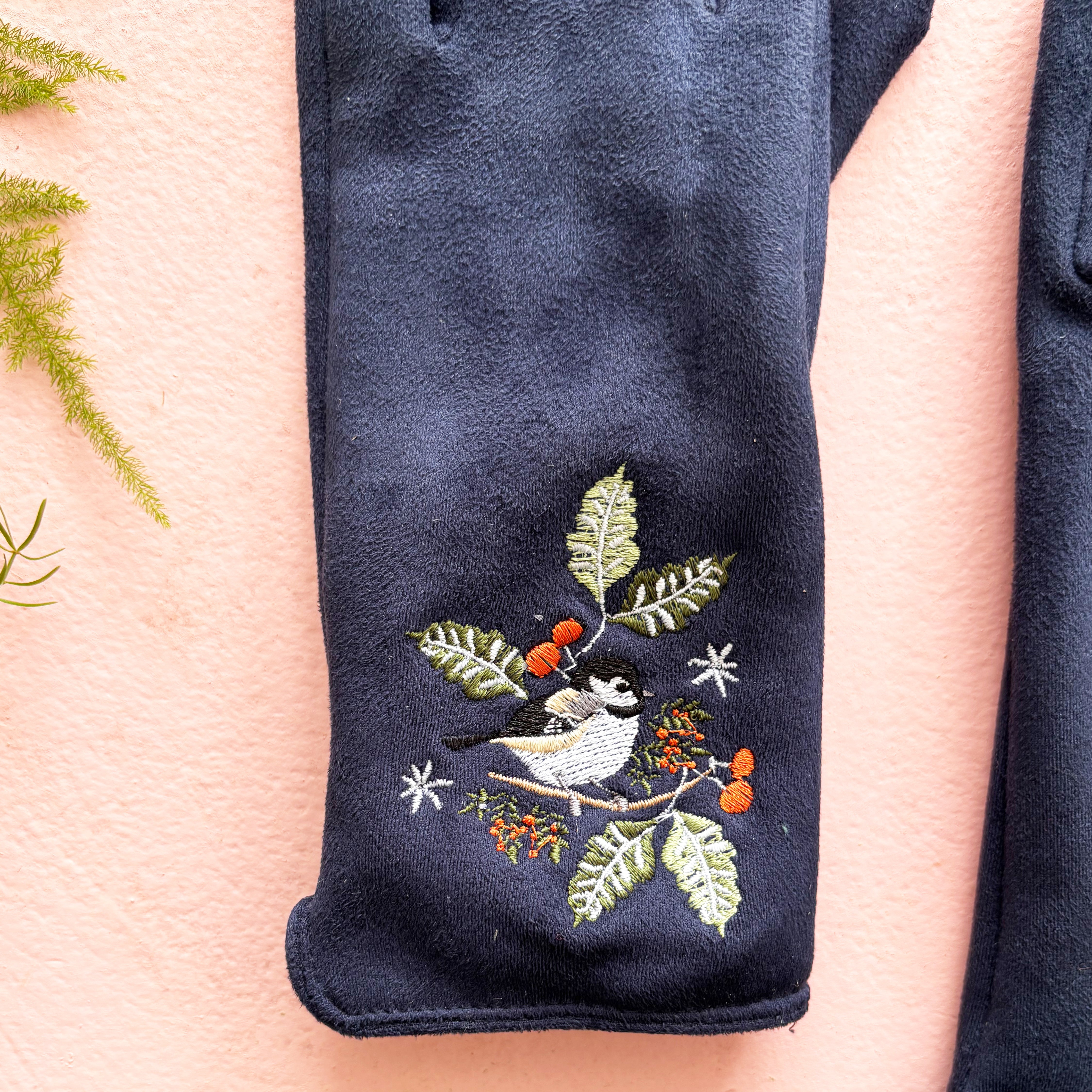 Close-up of embroidered bird perched among berries and leaves on navy suedette