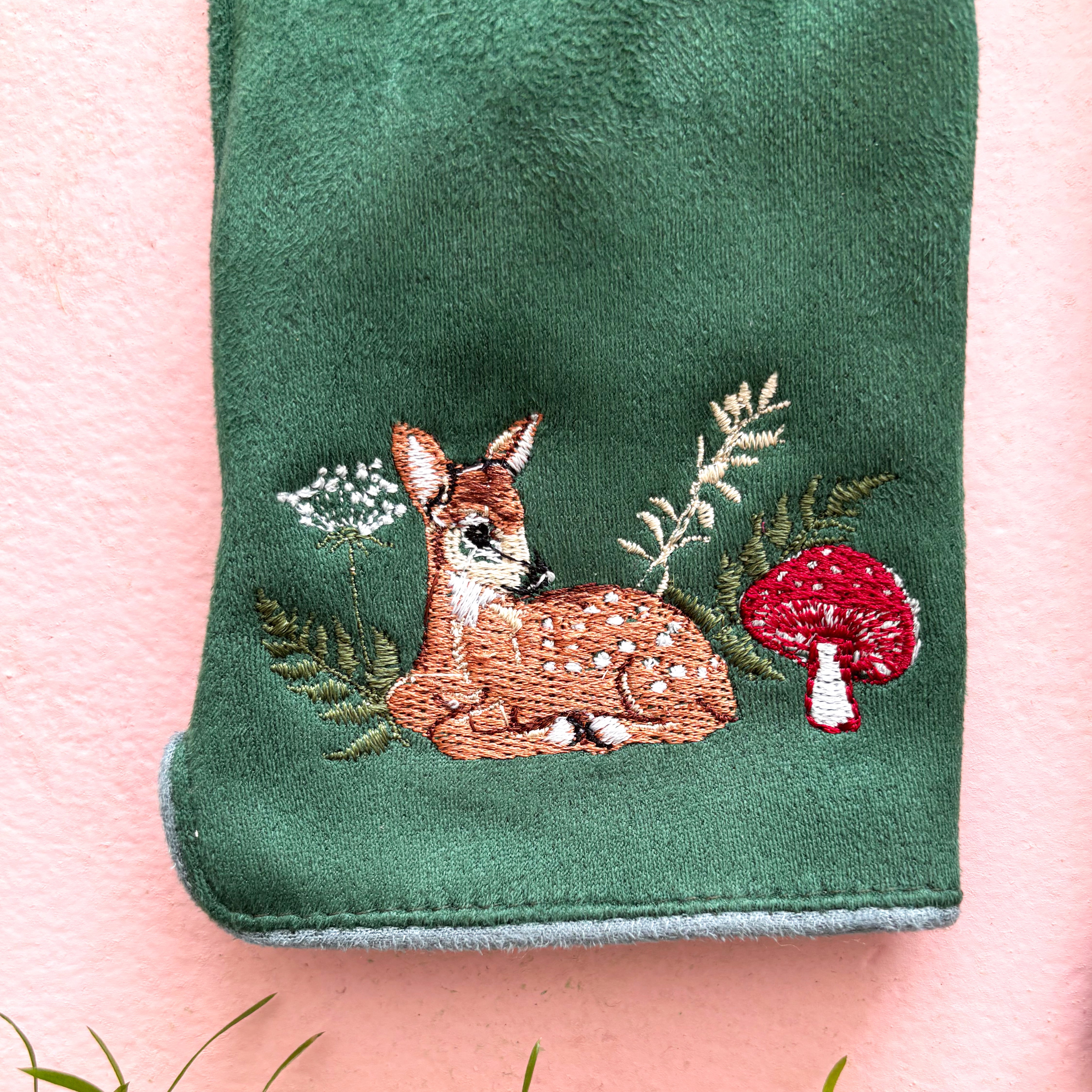 Close-up of embroidered fawn with toadstool mushroom on green glove cuff