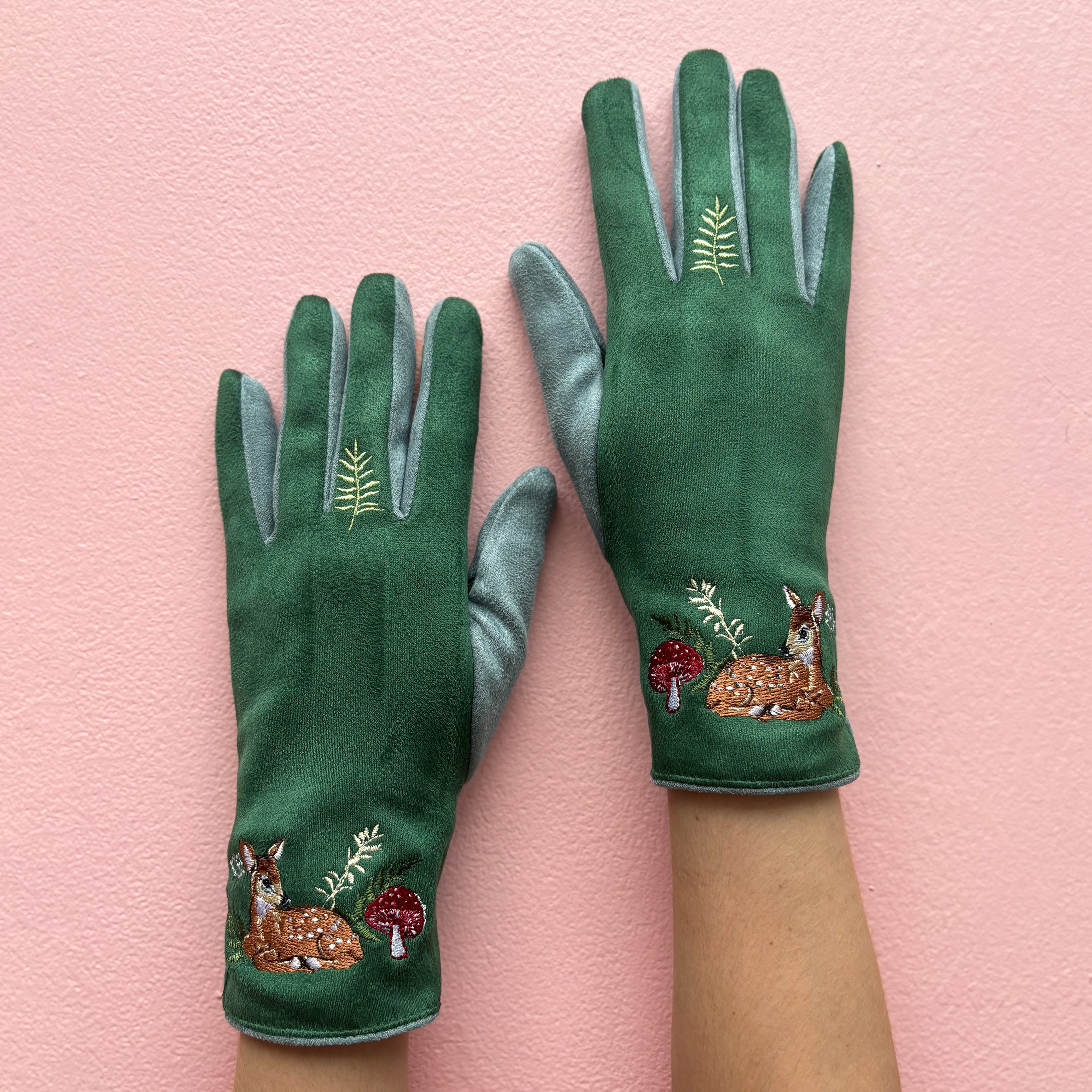 Green embroidered deer gloves worn on both hands against pink background