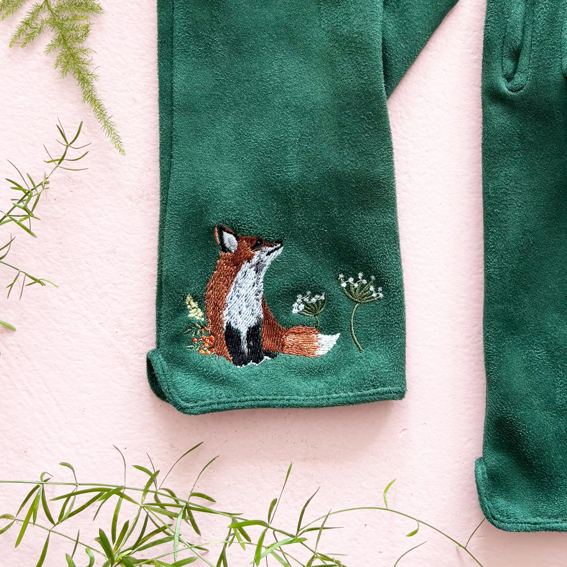 Close-up of embroidered fox nestled among wildflowers on green glove
