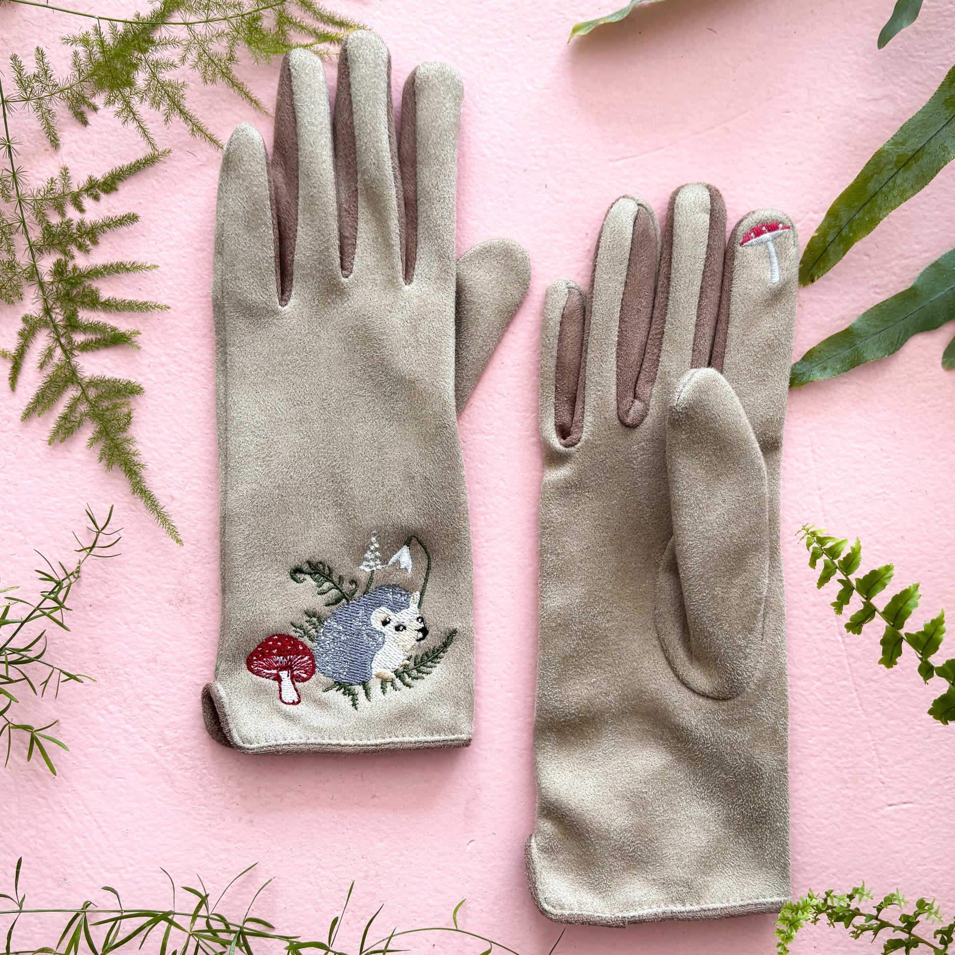 Both hedgehog gloves flat on pink background with greenery styling