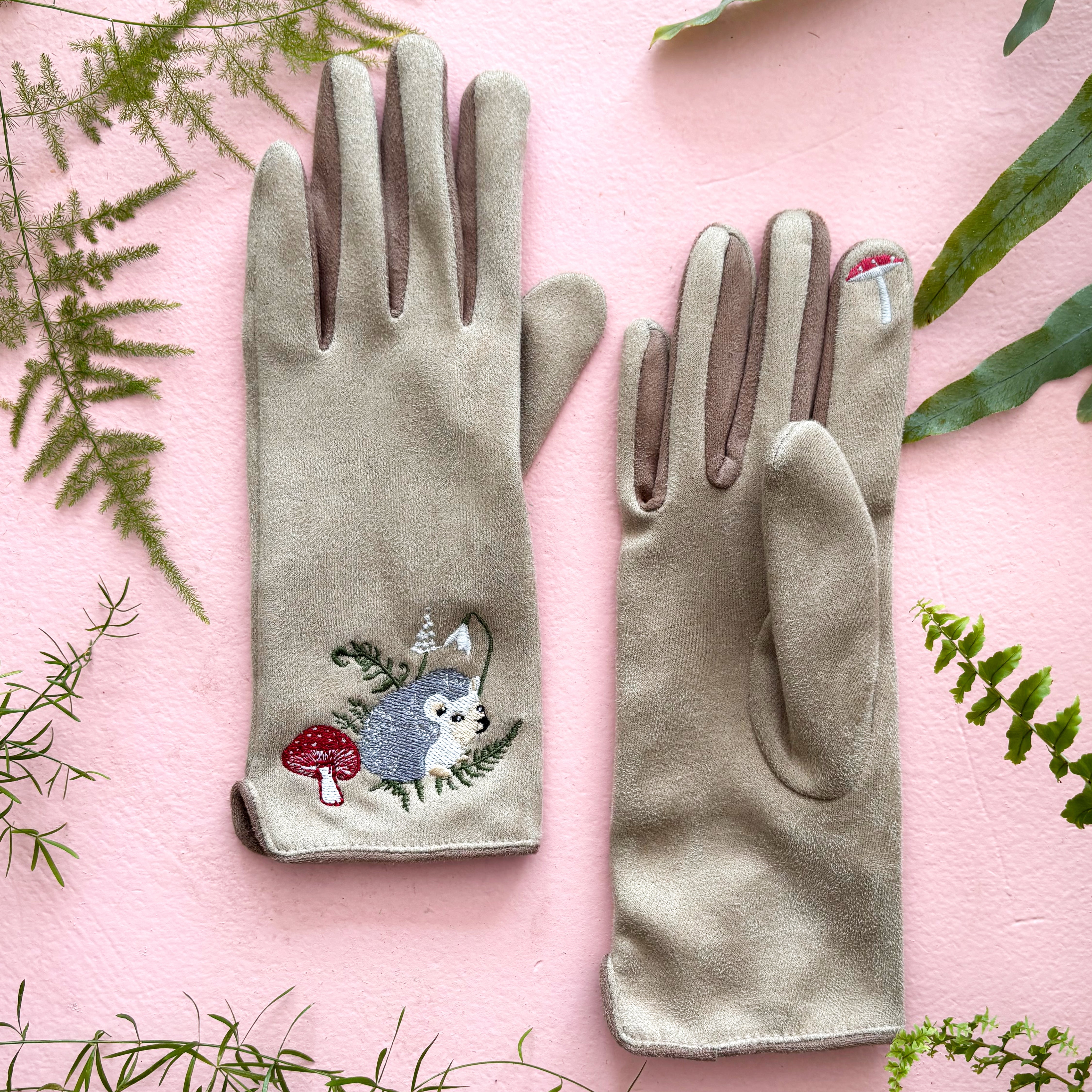 Both hedgehog gloves flat on pink background with greenery styling