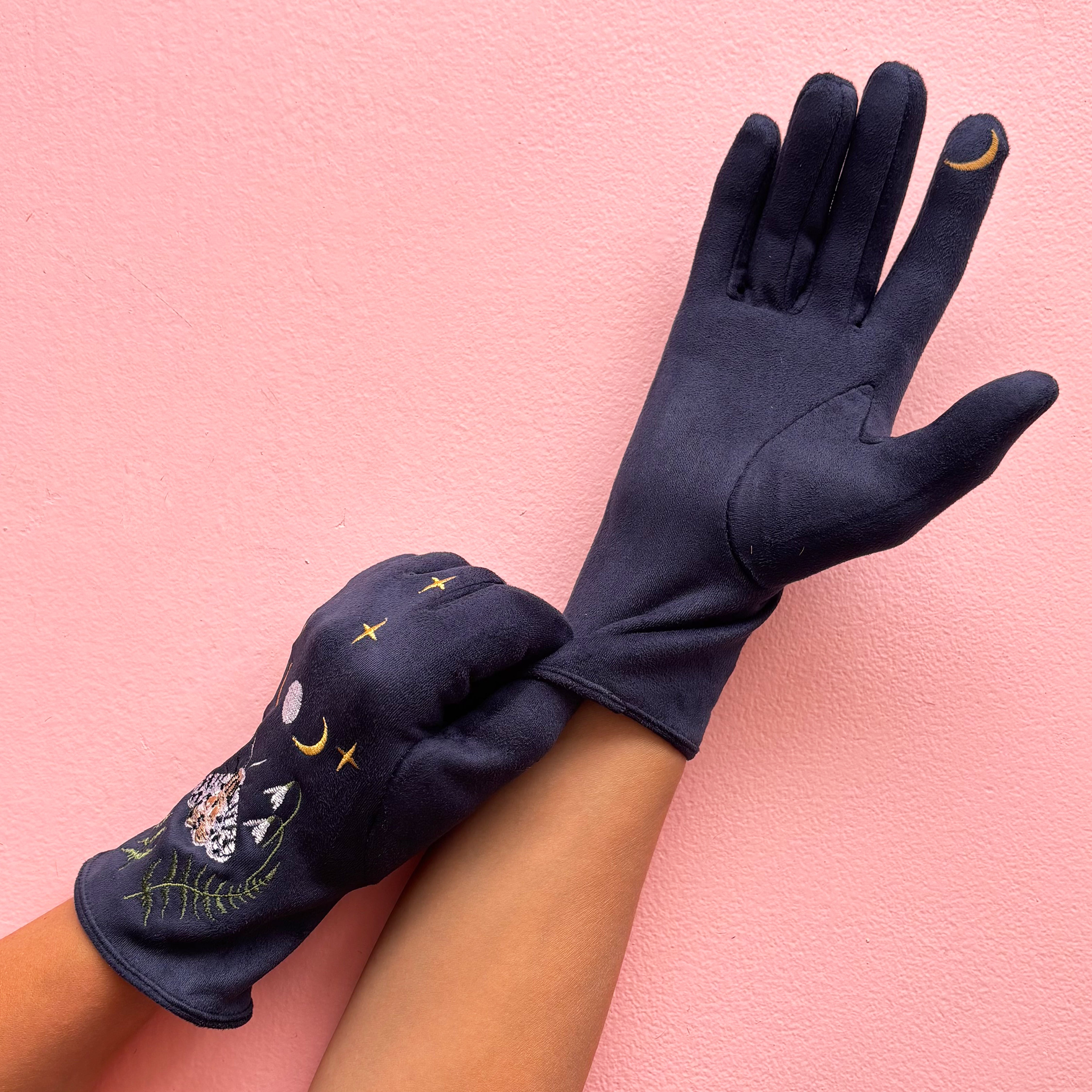 Back view of navy moth gloves worn on hand against pink background