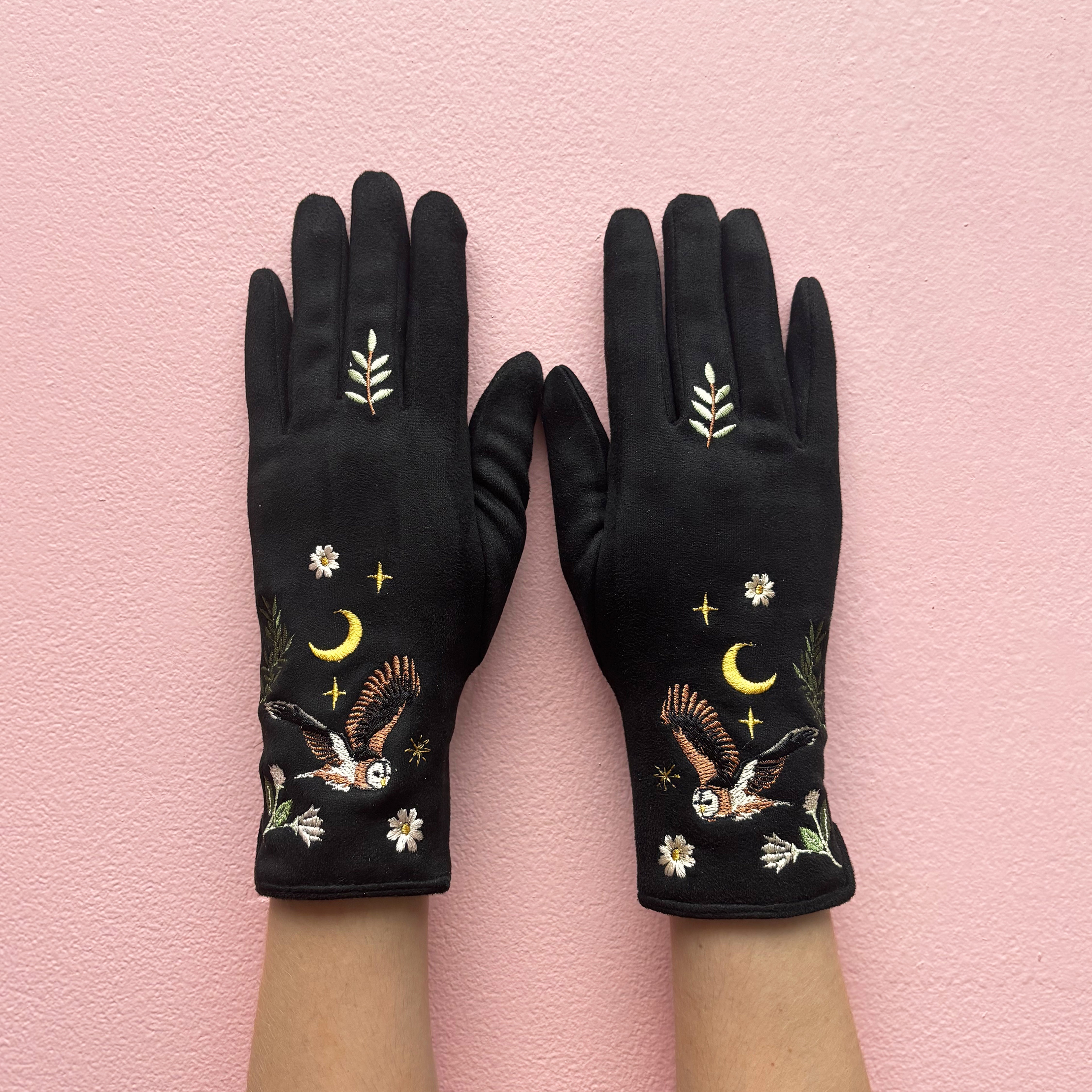 Black embroidered owl gloves worn on both hands against pink background